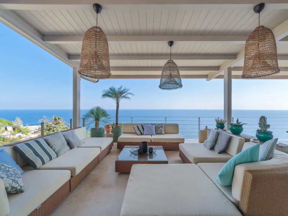 Open-air seating with sea views, wicker pendant lights, and cozy cushions at Villa Alba.