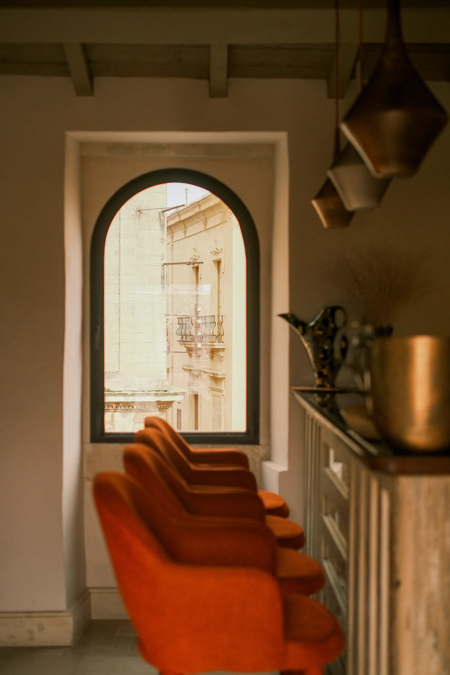 Interior bar area with terracotta walls, arched window and velvet bar stools overlooking a historic Italian palazzo