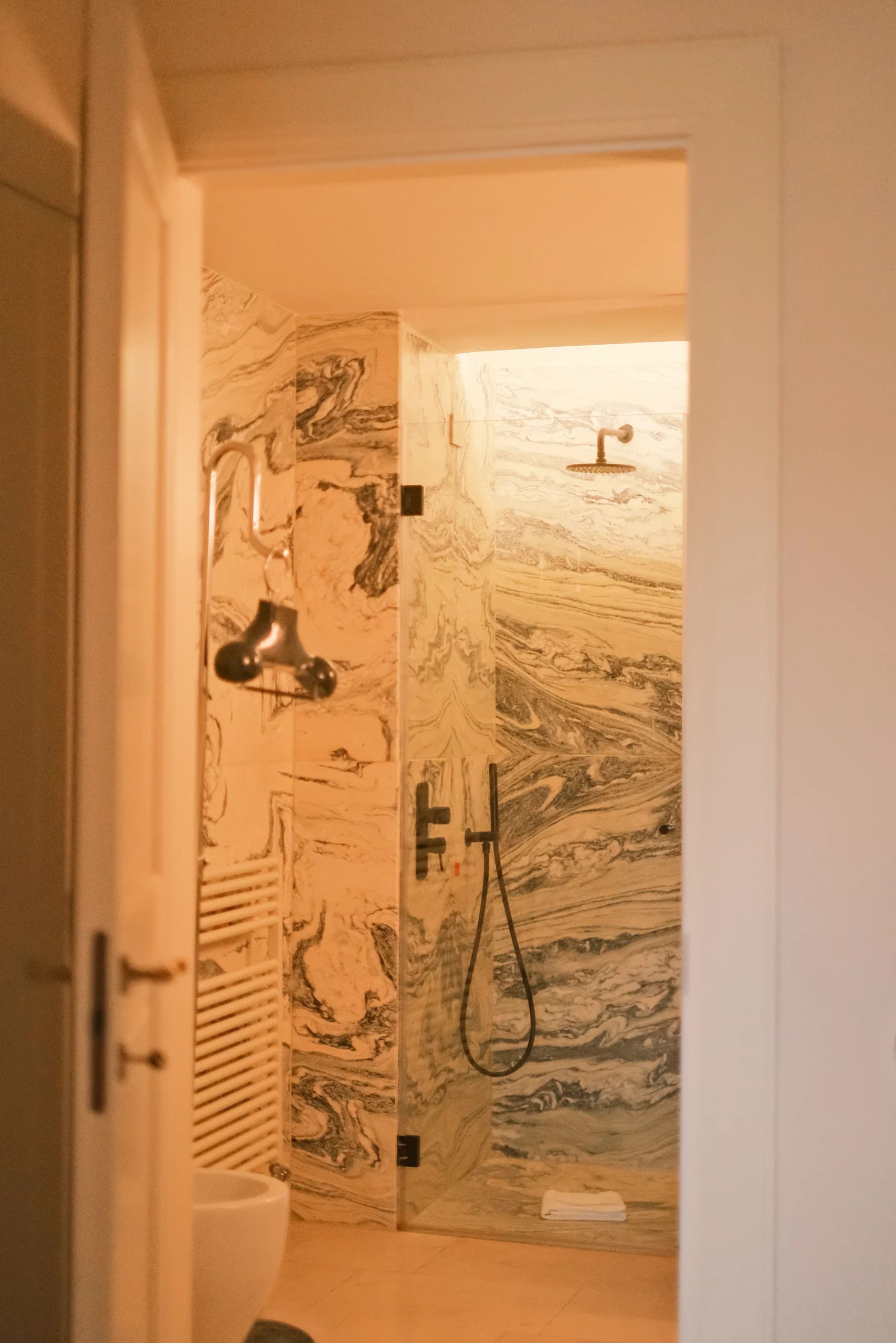 Luxury marble walk-in shower with natural stone walls and minimalist black fixtures in a refined Italian bathroom
