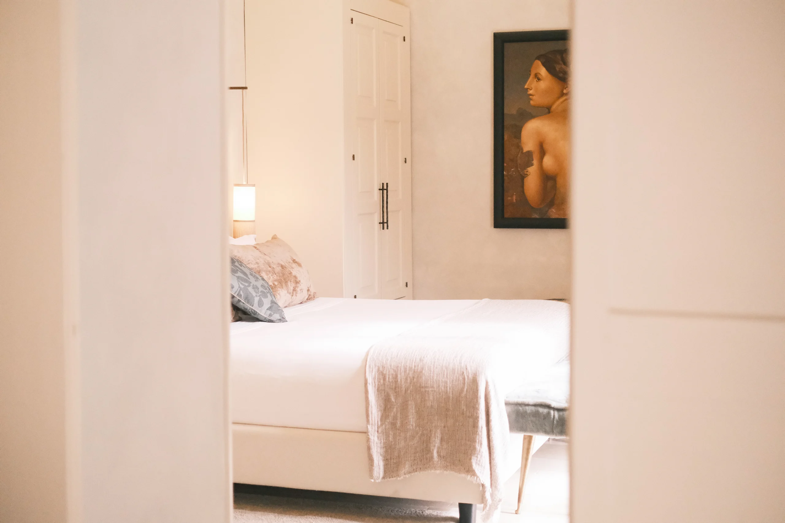 Elegant bedroom view through doorway with soft lighting, refined textiles, and art details