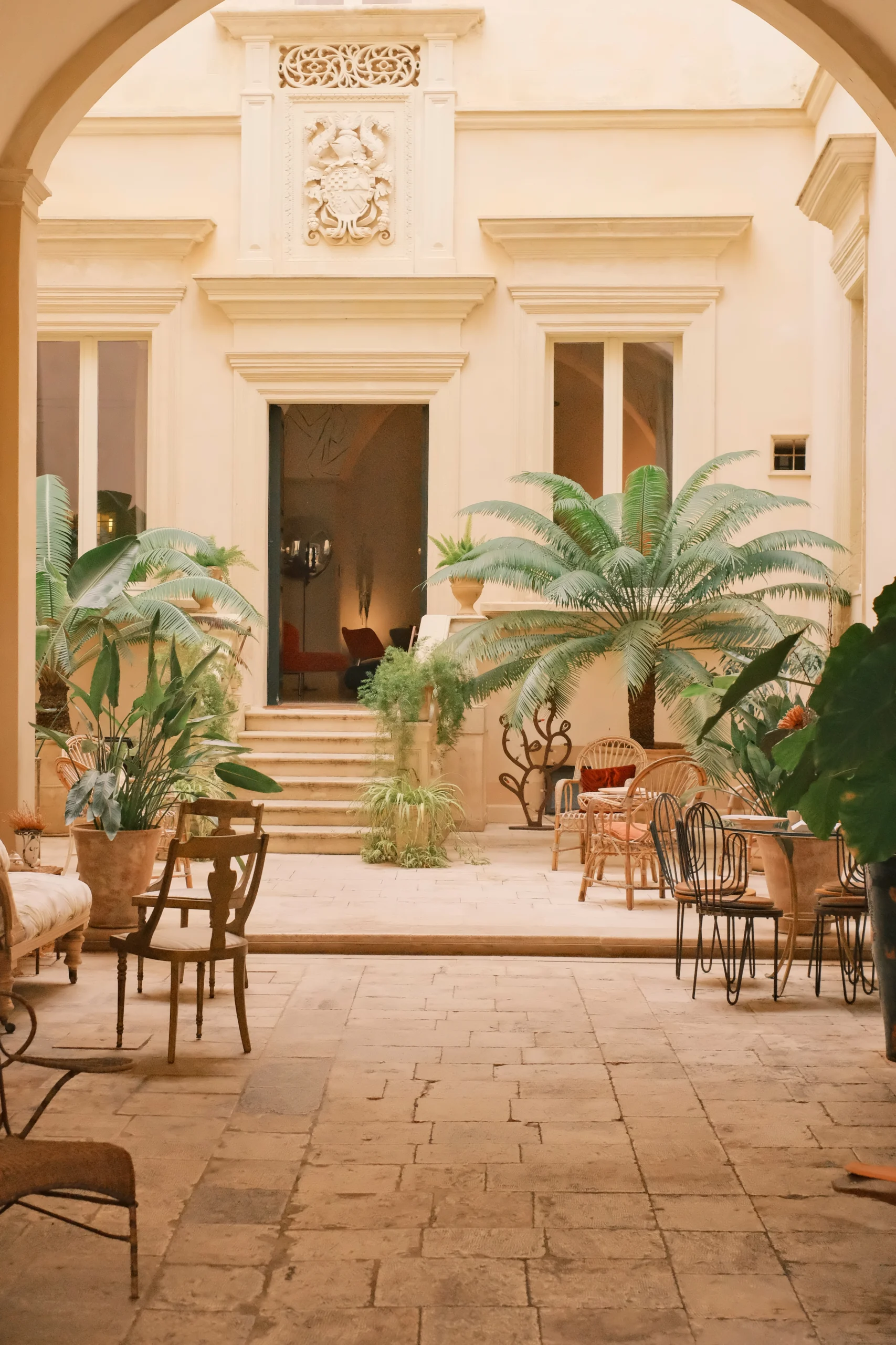 Luxury palazzo courtyard with palm trees, outdoor seating, and arched architectural details in Puglia