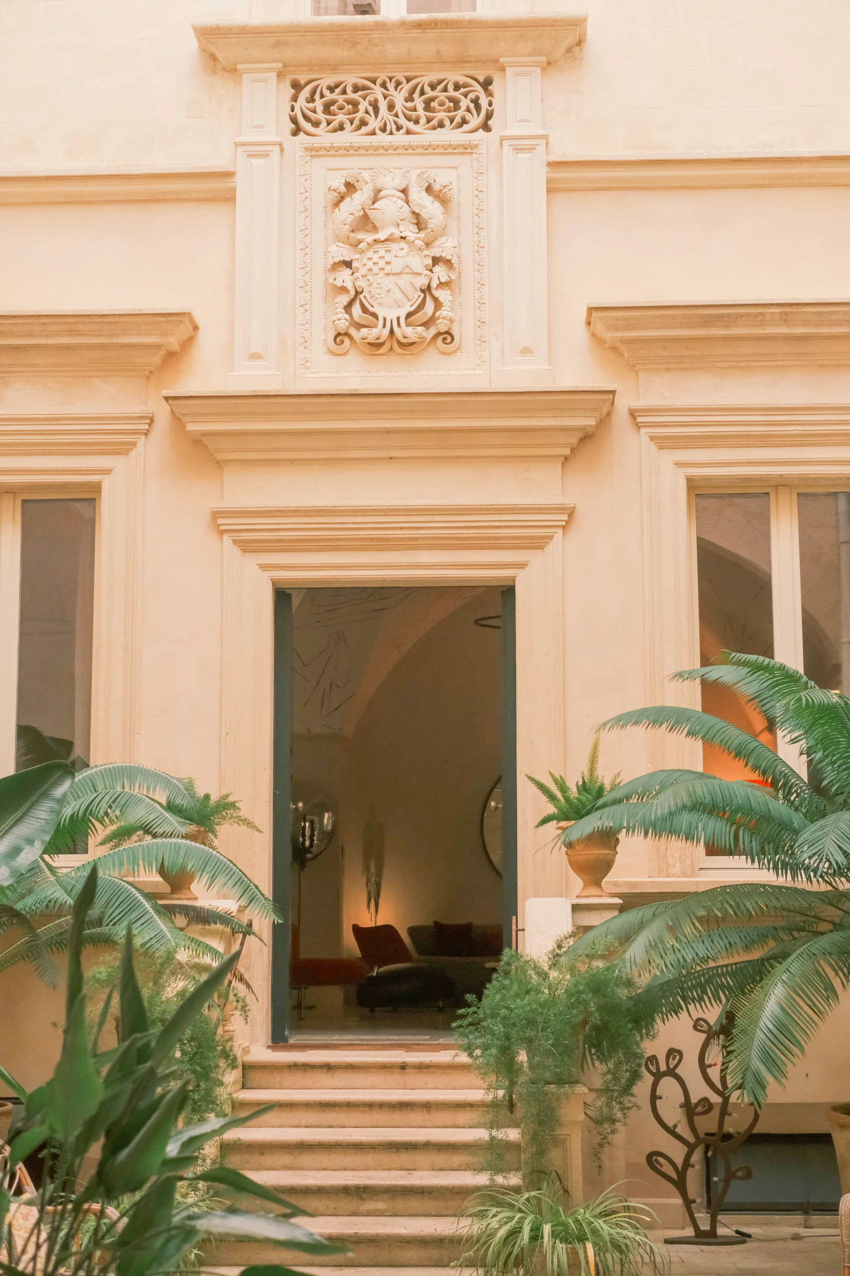 Grand courtyard entrance with sculpted stone façade, palm trees, and symmetrical architecture in Puglia