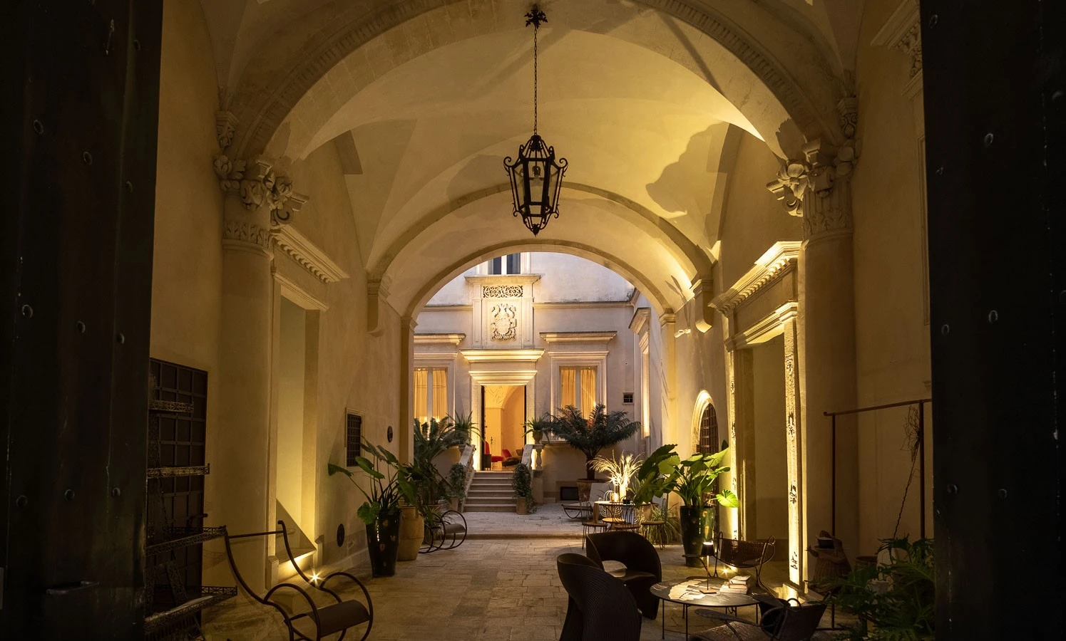 Historic palazzo courtyard in Puglia with vaulted stone arches, soft lighting, lounge seating and Mediterranean plants at night