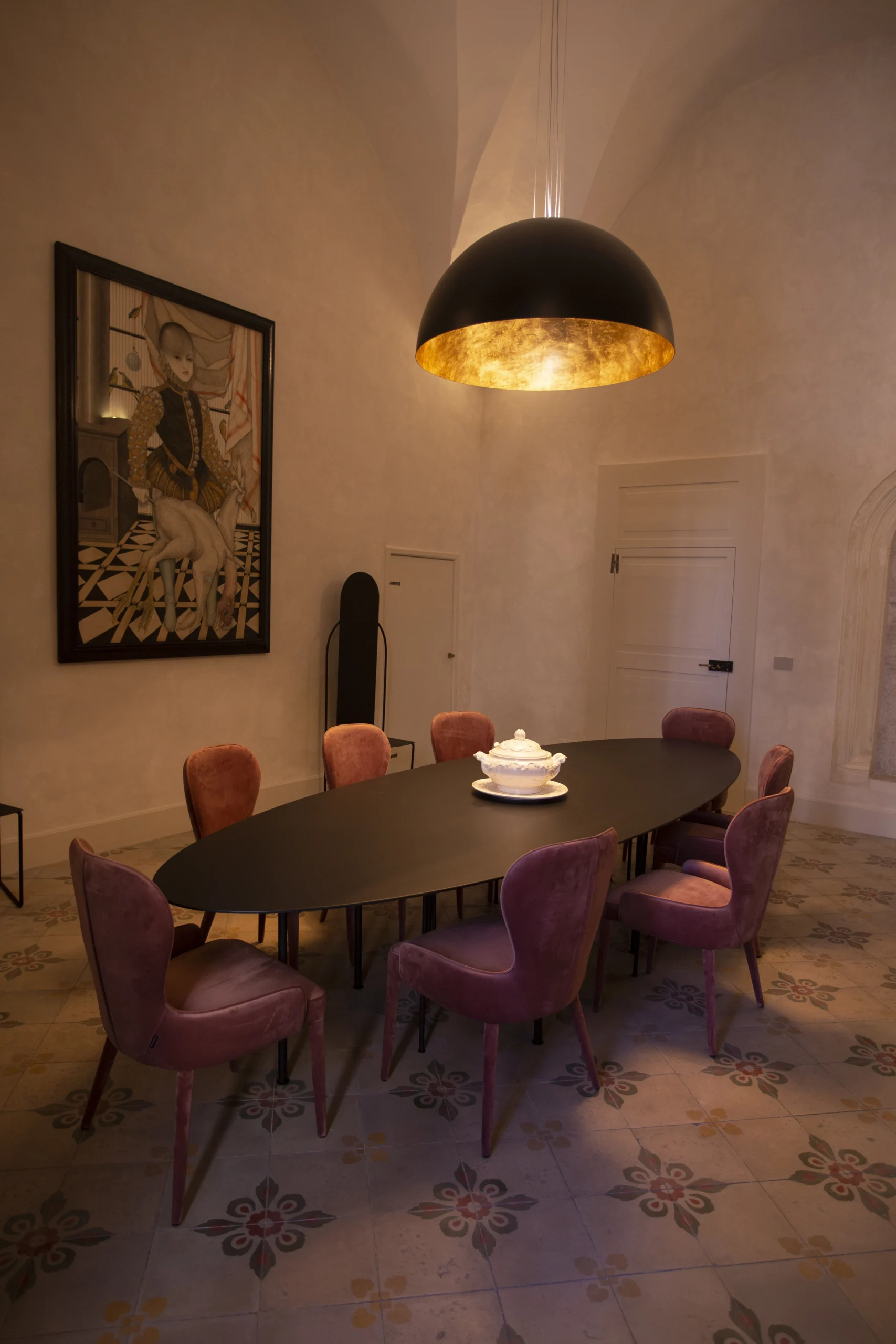 Elegant dining room with large oval table, velvet chairs, designer pendant light and patterned tile floor in Italian palazzo