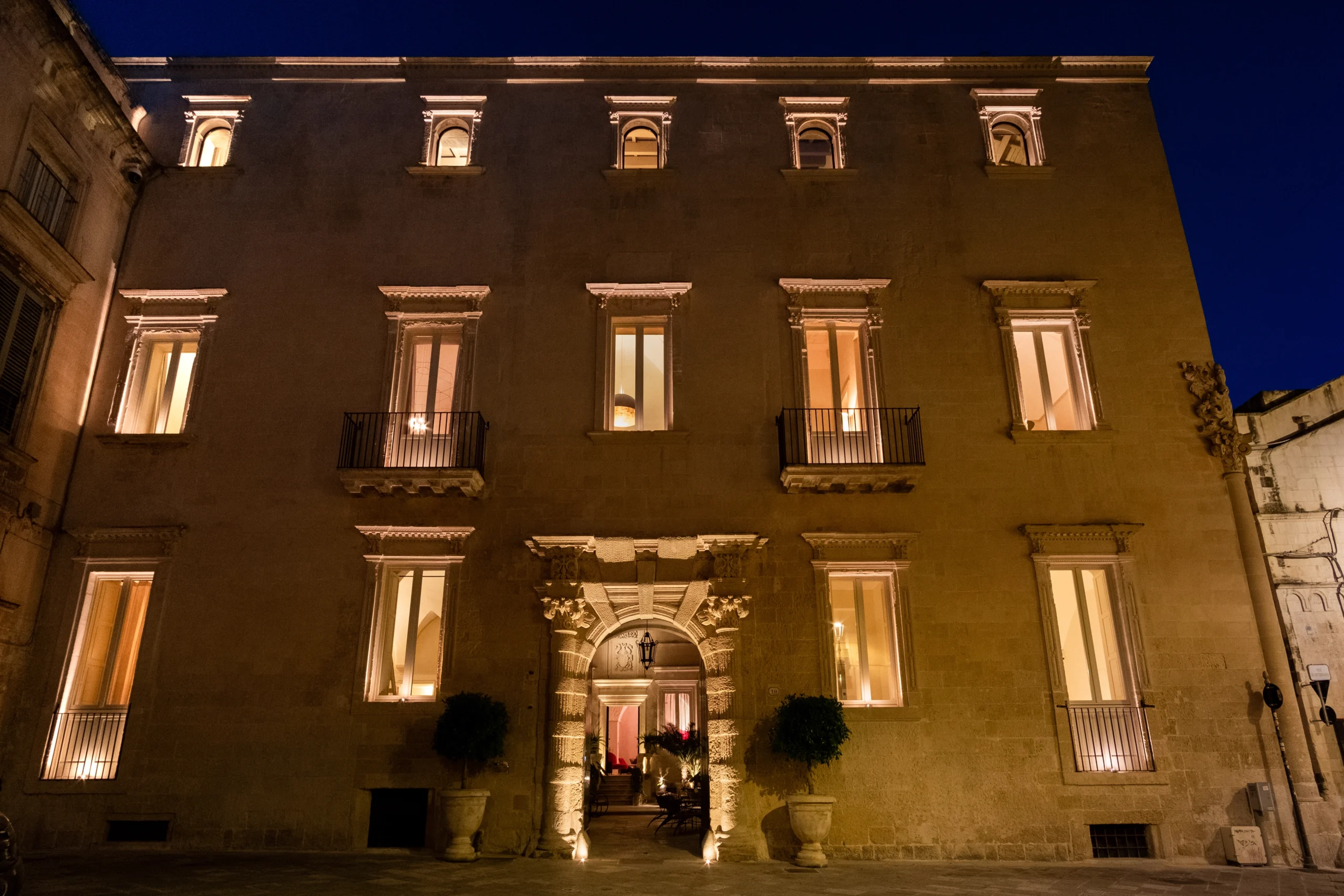 Night view of a historic palazzo facade with illuminated windows and central entrance in Lecce, Puglia