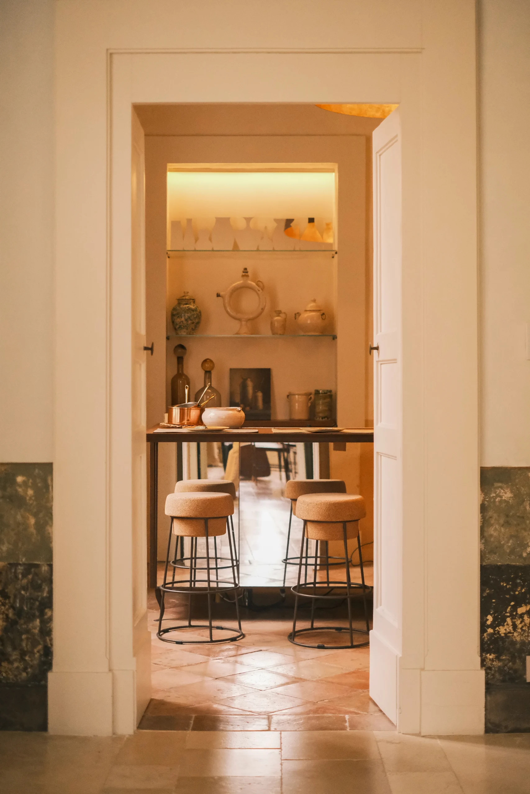 View through a doorway into a refined kitchen bar area with stools and ceramic decor in a luxury palazzo, Puglia