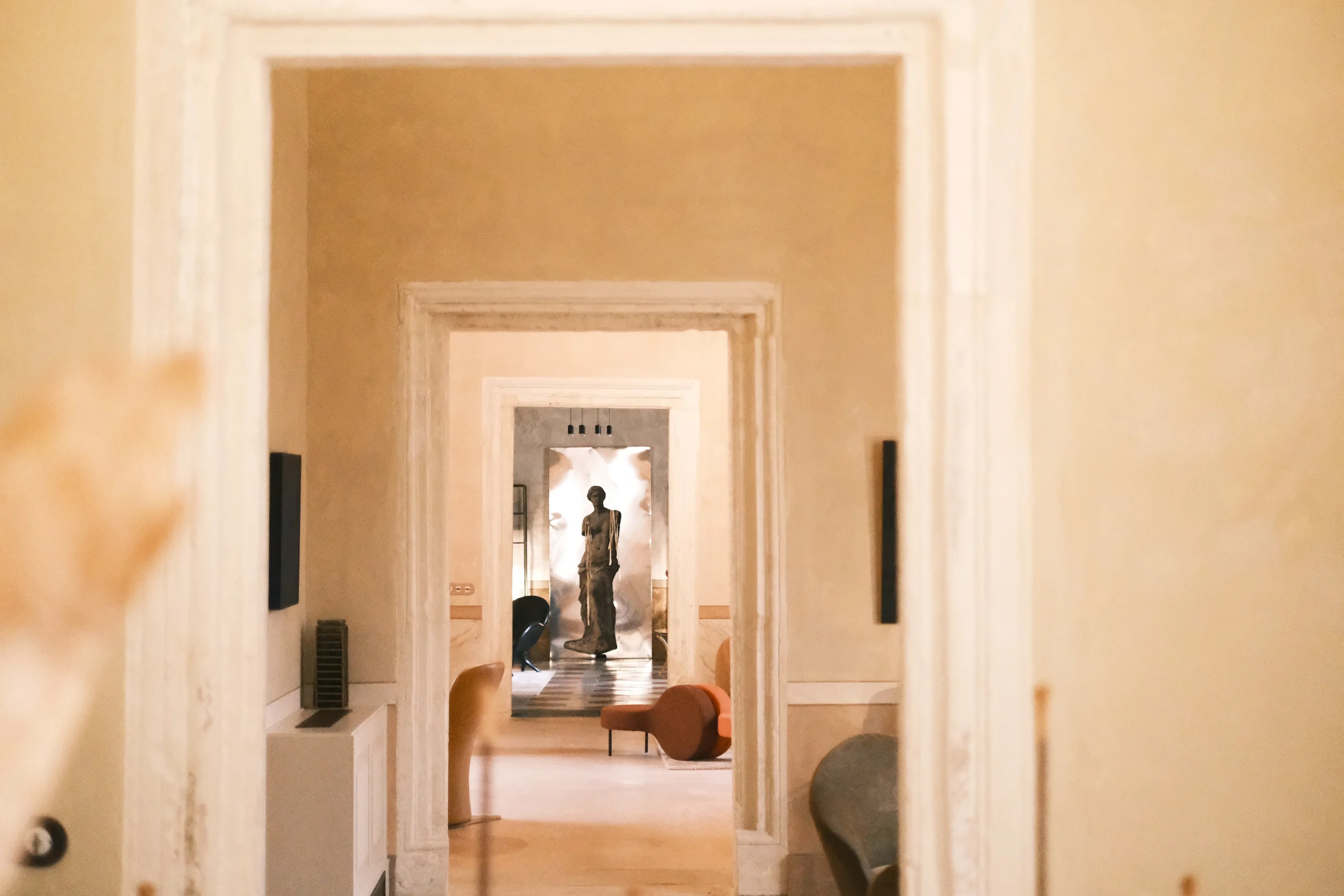 Elegant enfilade view through historic doorways revealing a refined living room with sculptural furniture and contemporary art in a luxury palazzo in Puglia