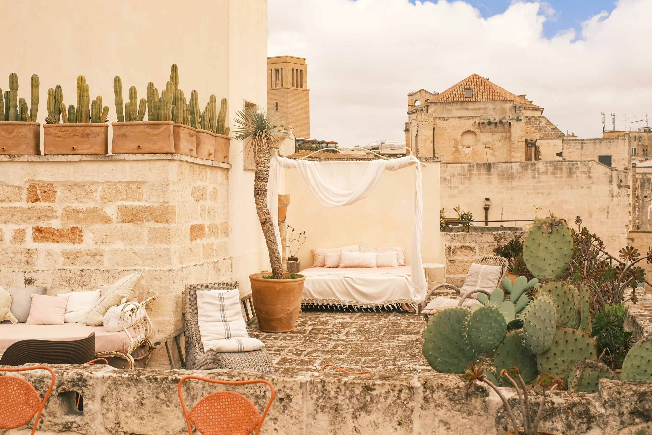 Rooftop terrace with daybed, potted cacti and historic stone walls overlooking the old town of Lecce, Puglia