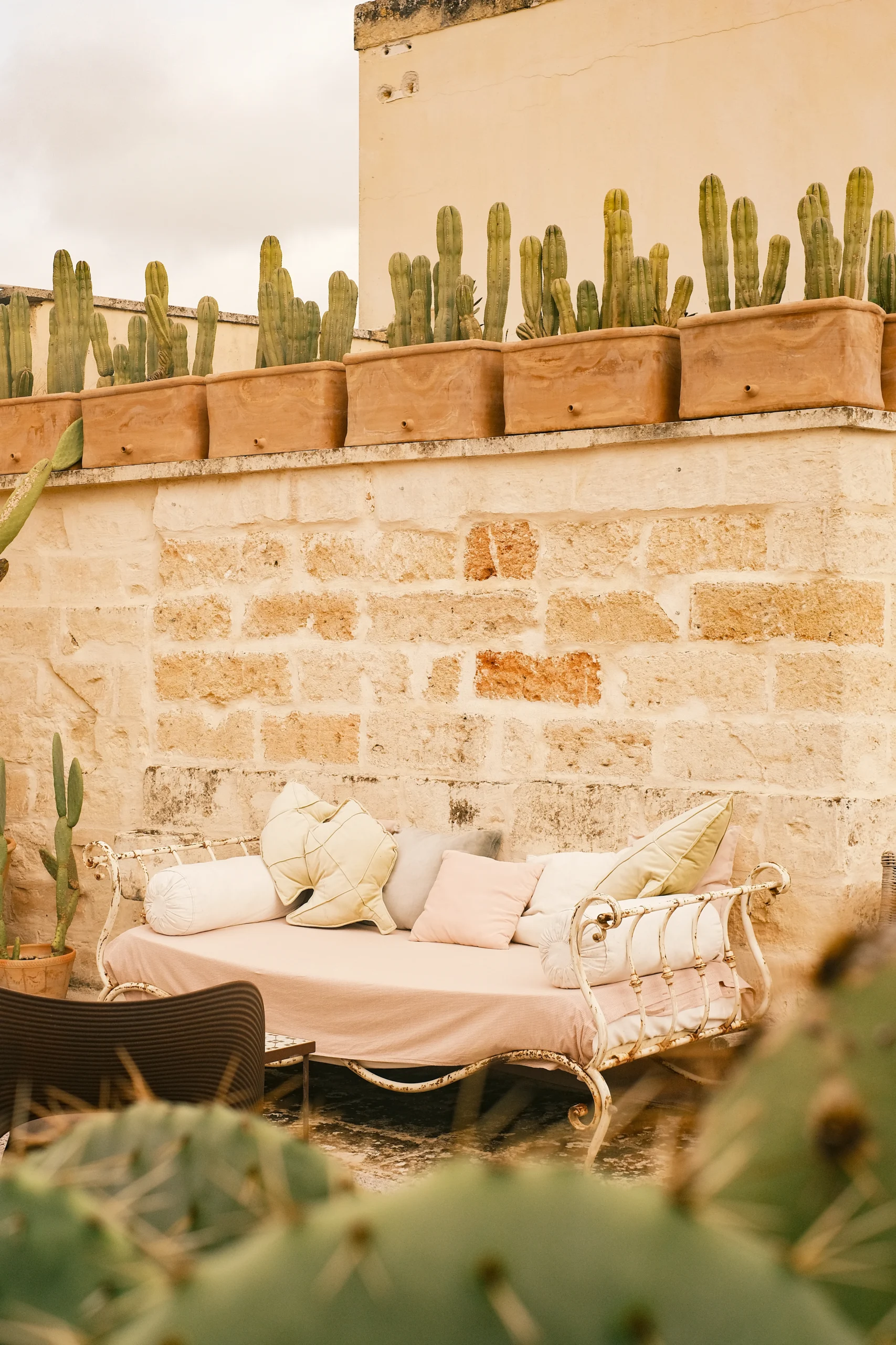 Detail of rooftop lounge with vintage daybed, soft cushions and stone walls surrounded by Mediterranean plants in Lecce