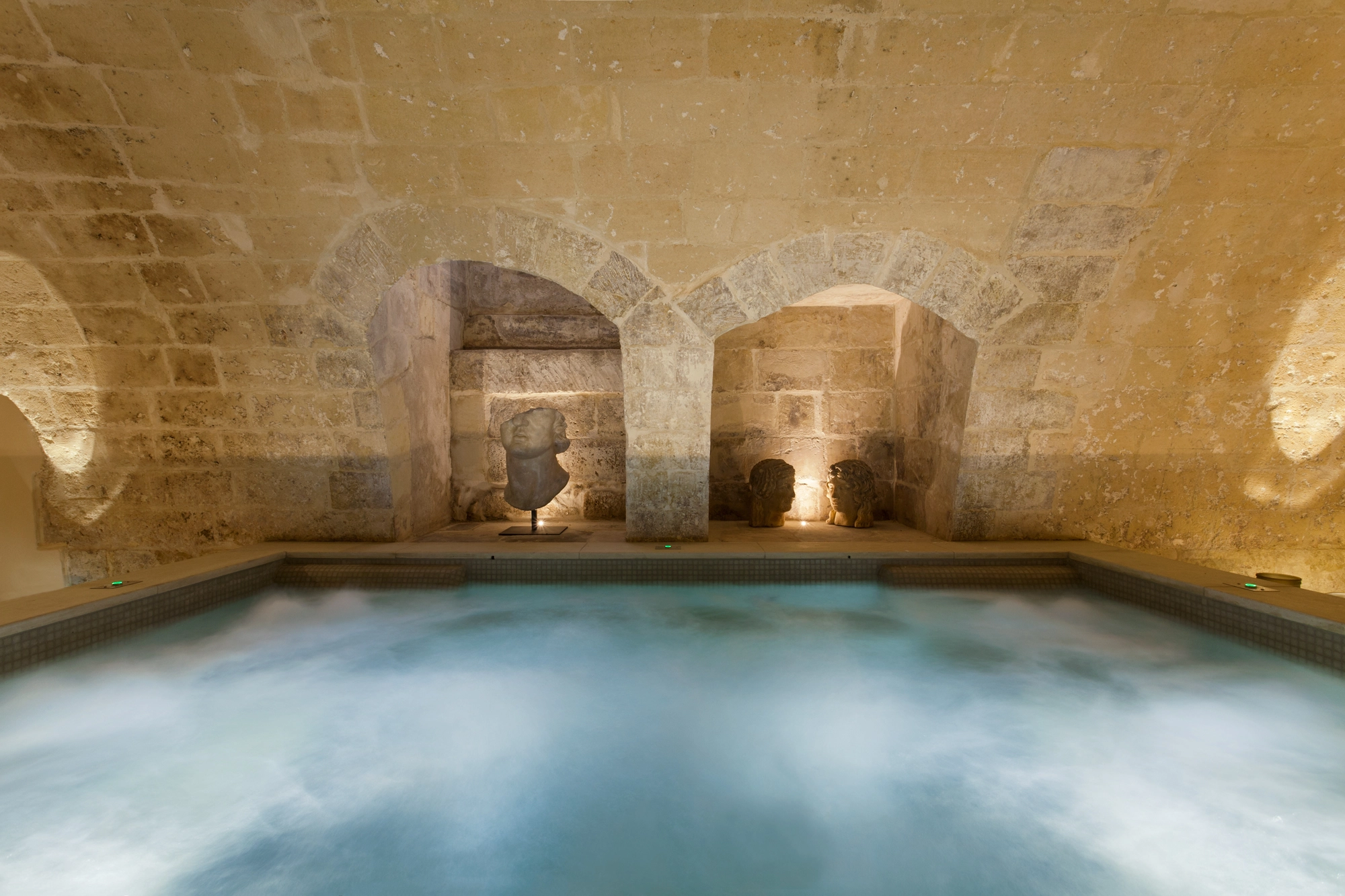 Sculptural stone niches and classical busts surrounding an indoor pool in a luxury spa