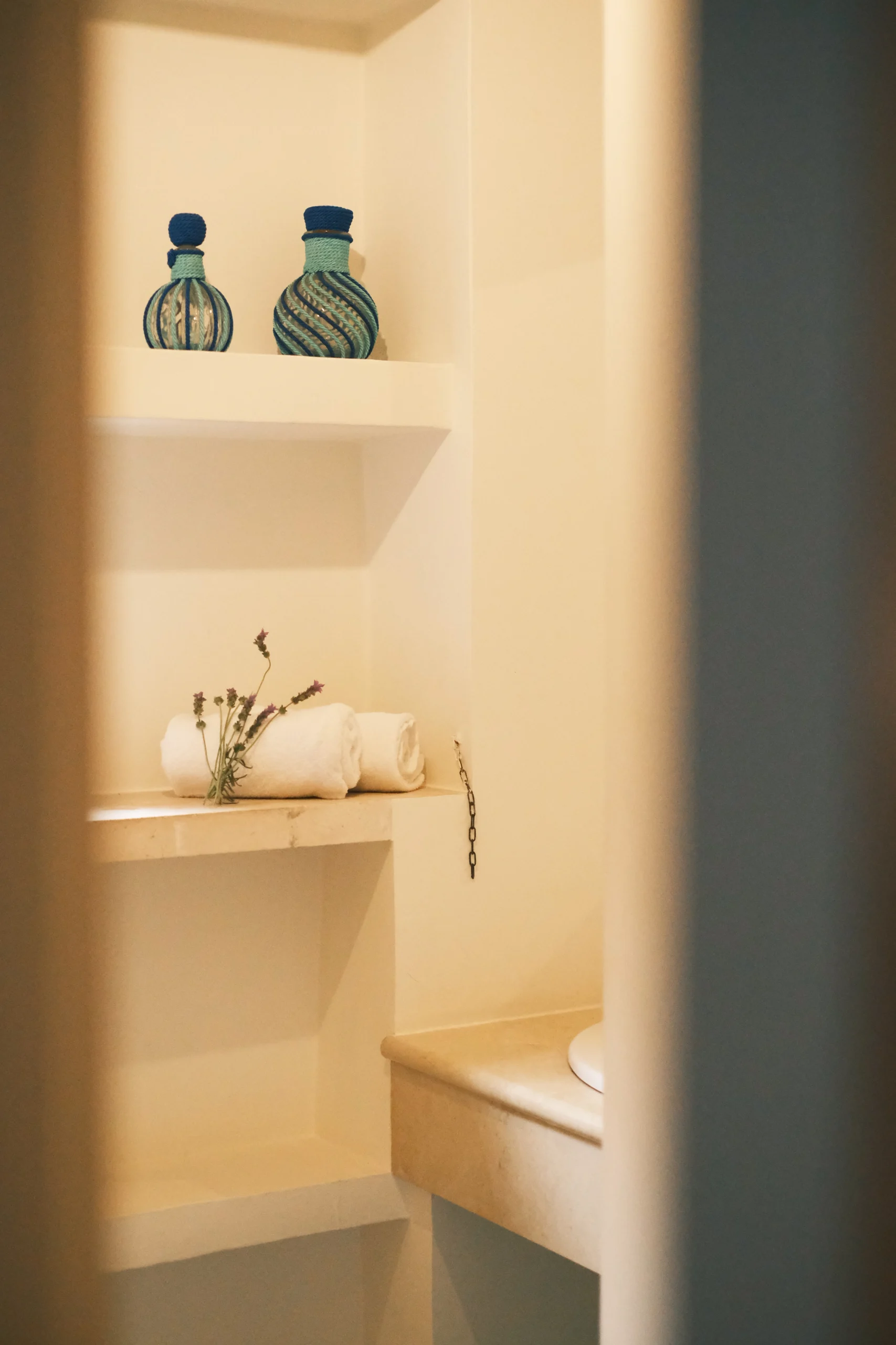 Bathroom shelf detail with folded towels and decorative glass bottles at luxury villa in Puglia