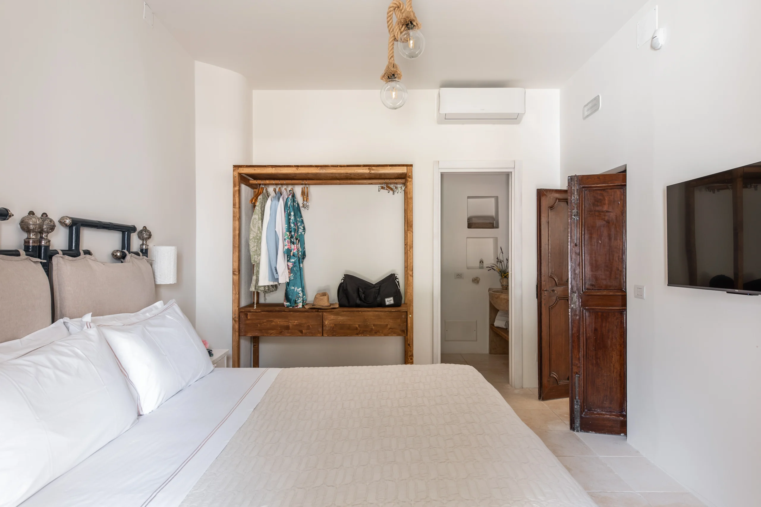 Bright double bedroom with natural fabrics, open wardrobe and en-suite bathroom at luxury villa in Puglia