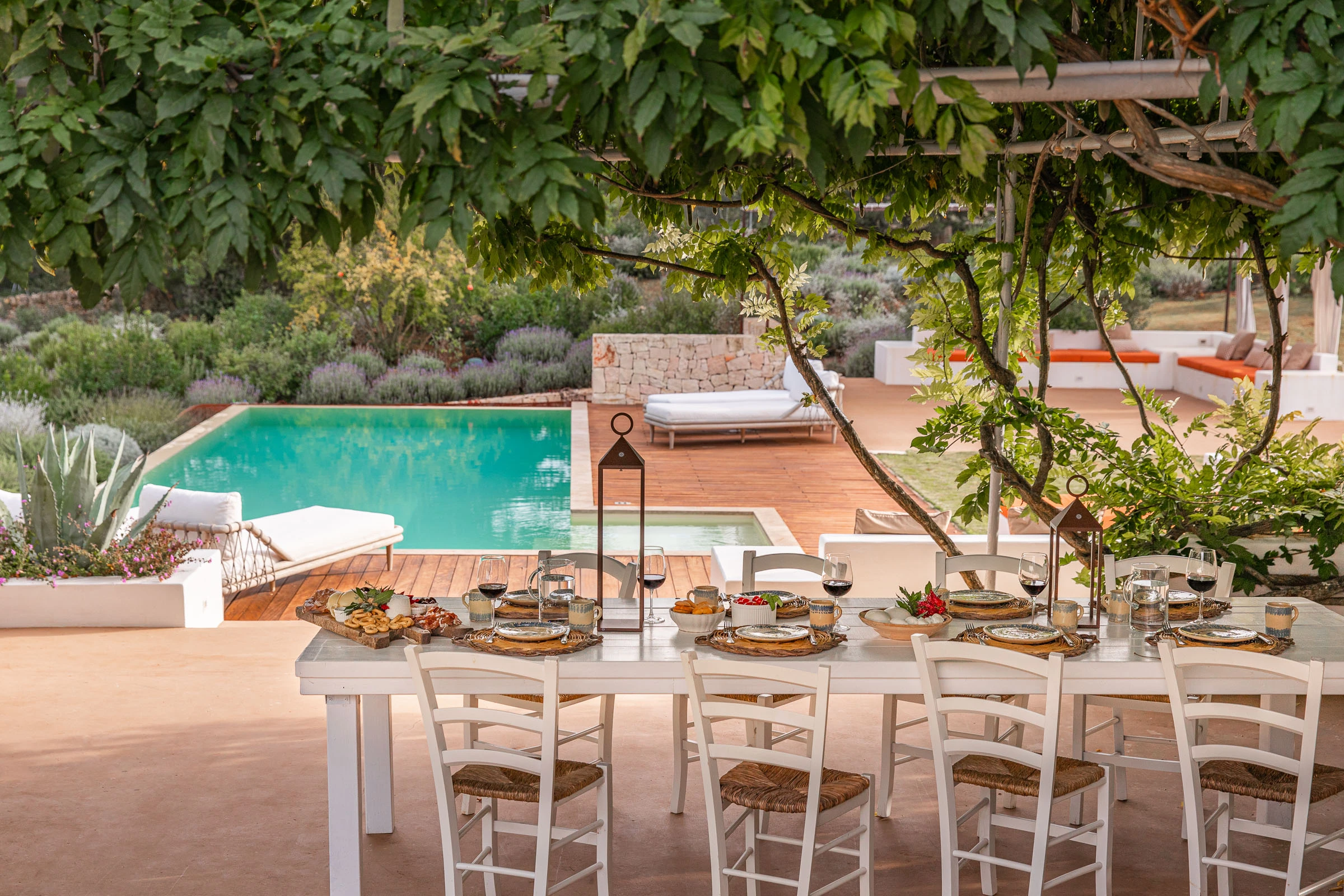 Long outdoor dining table set for an al fresco meal under a pergola, overlooking the garden and swimming pool in Puglia