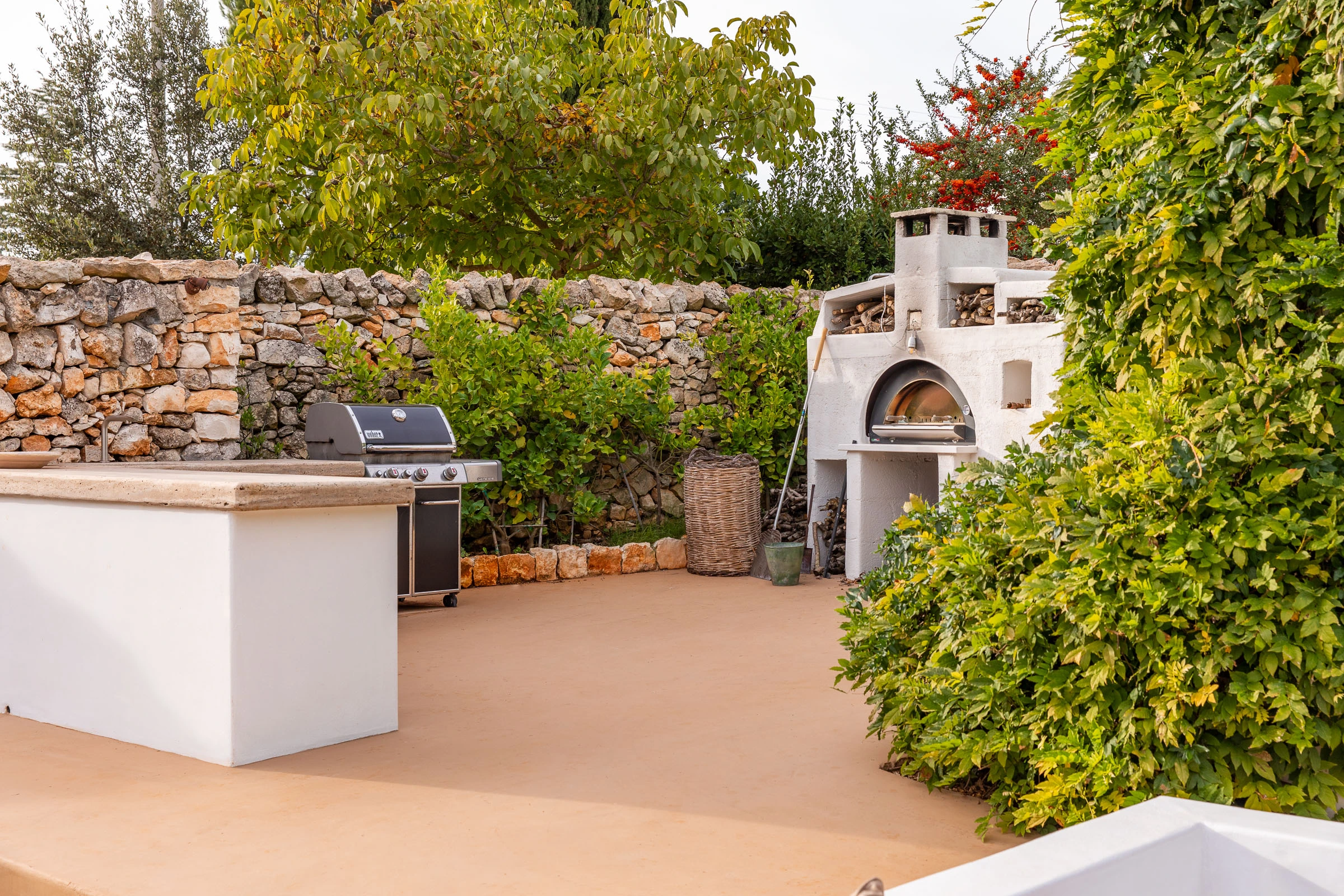 Outdoor kitchen area with built-in barbecue and pizza oven, set in a landscaped garden in Puglia