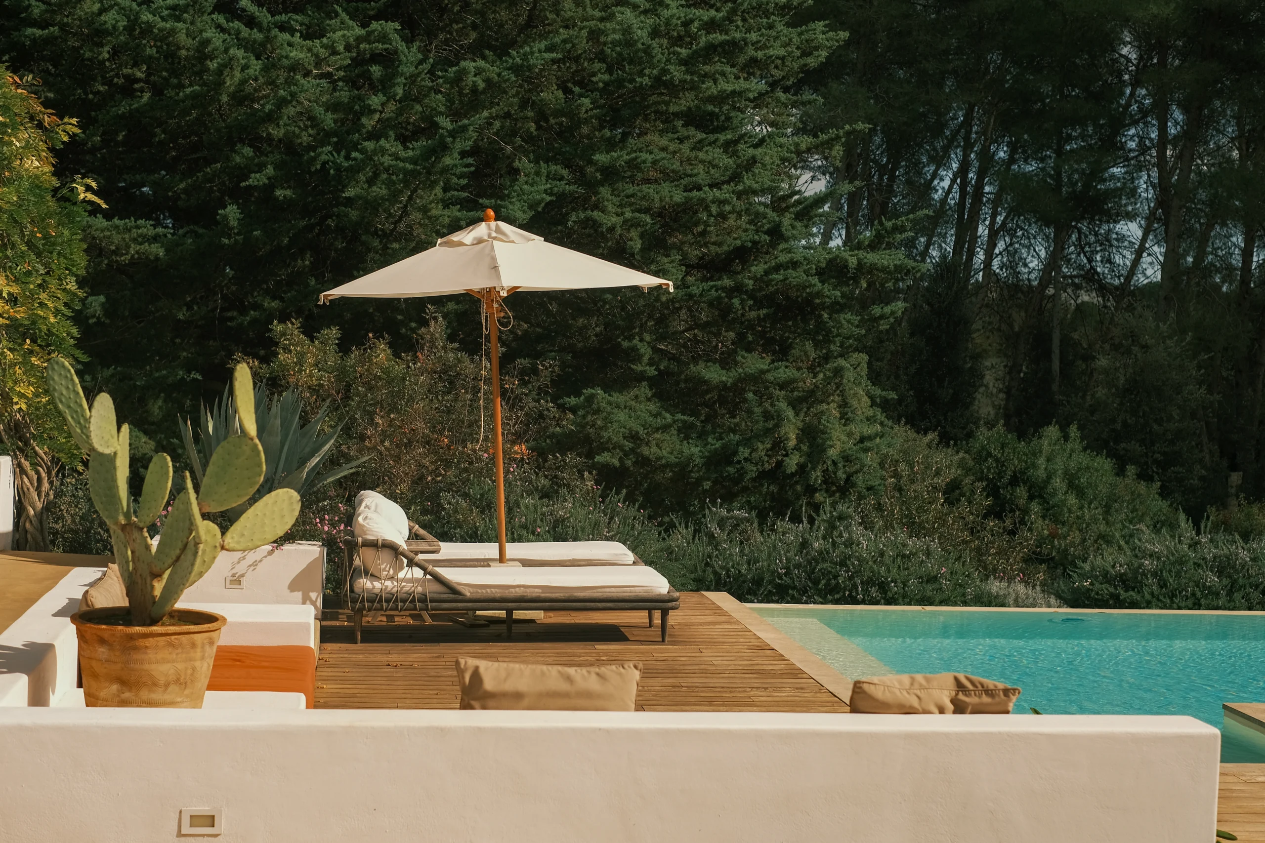 Poolside relaxation area with cactus plants, wooden deck and parasol in a private Puglia villa