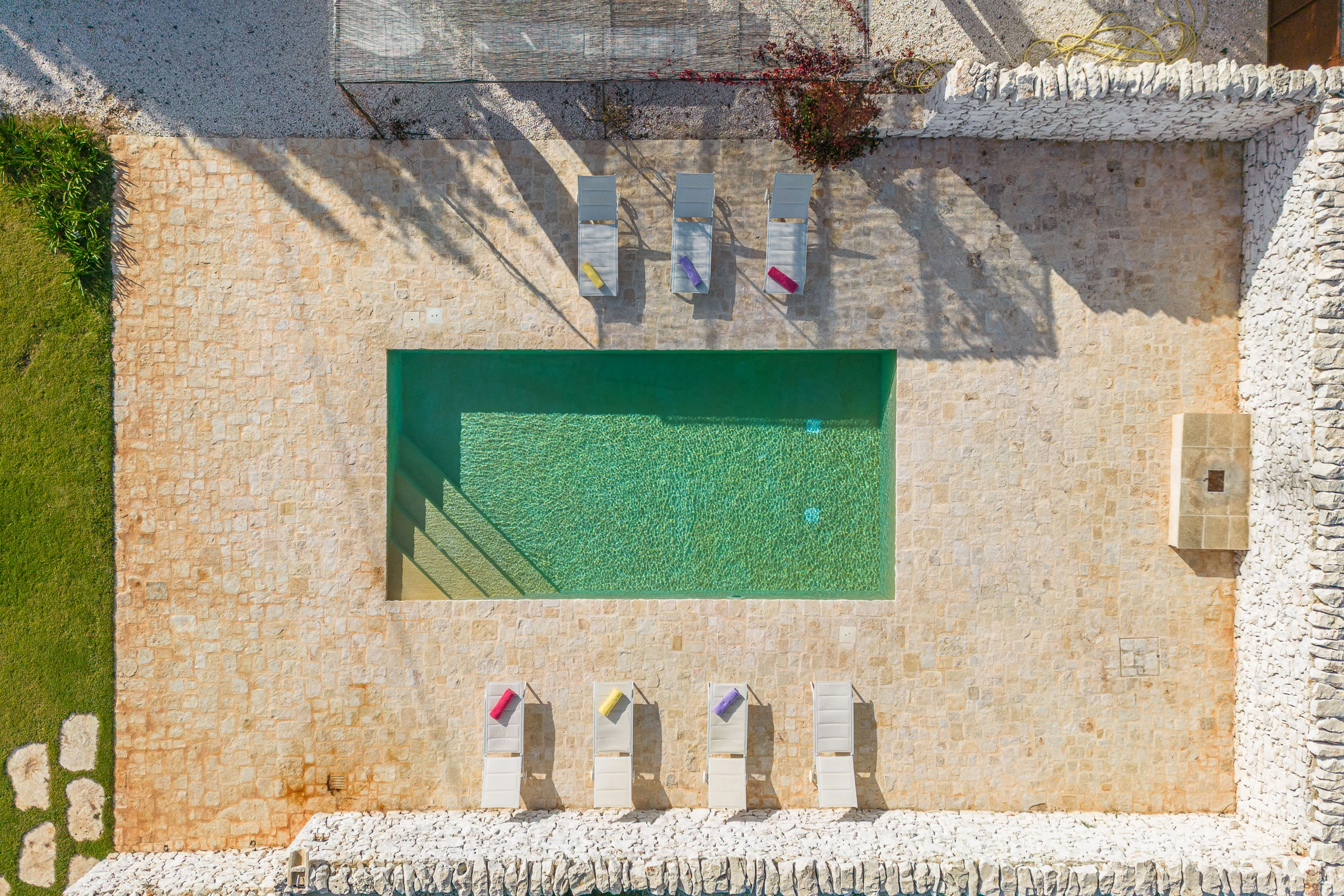 Aerial view of a rectangular swimming pool with sun loungers set in a stone courtyard in Puglia