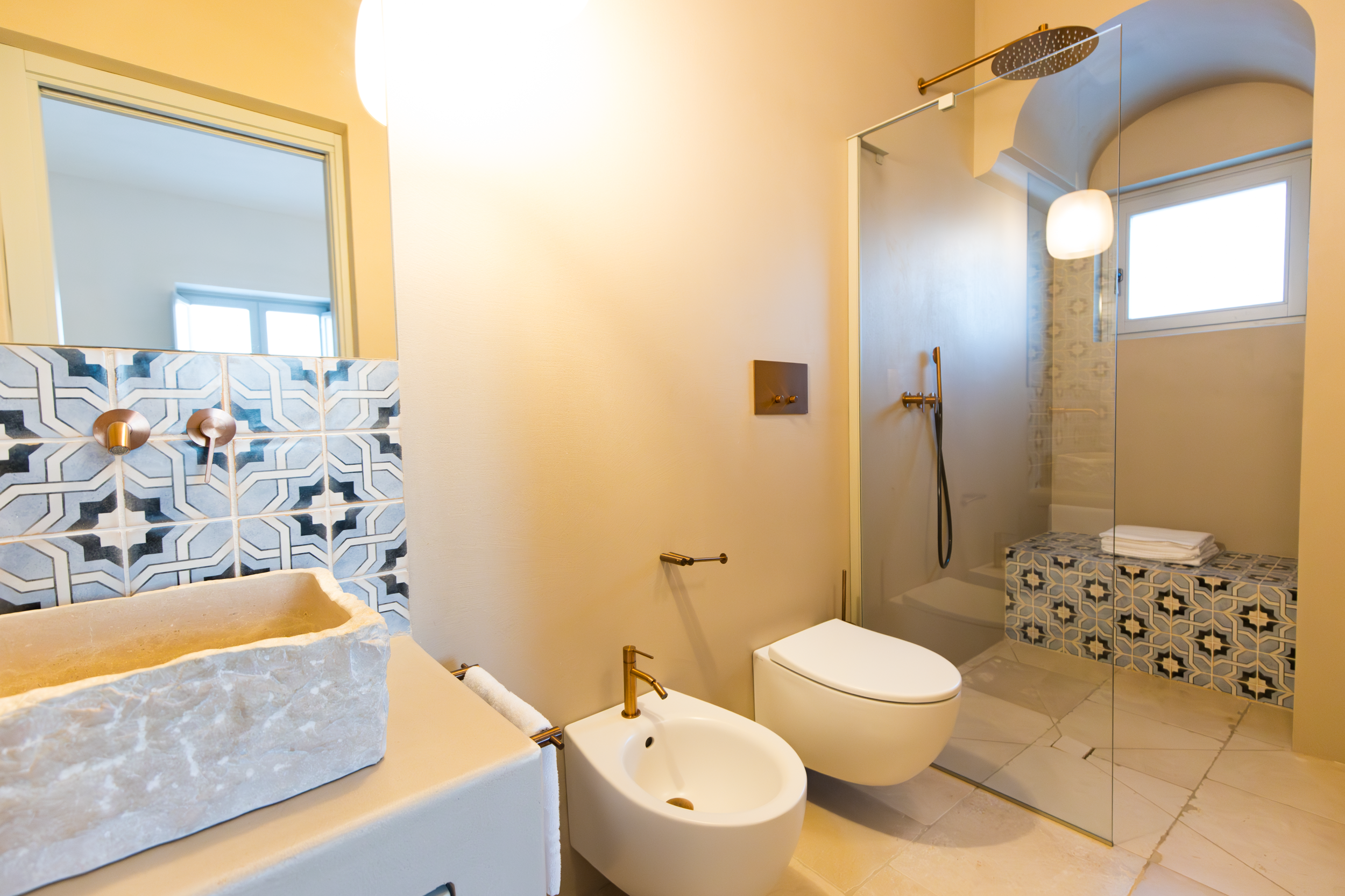 Spacious bathroom with walk-in shower, stone basin, bidet and patterned tiles in a private villa in Puglia
