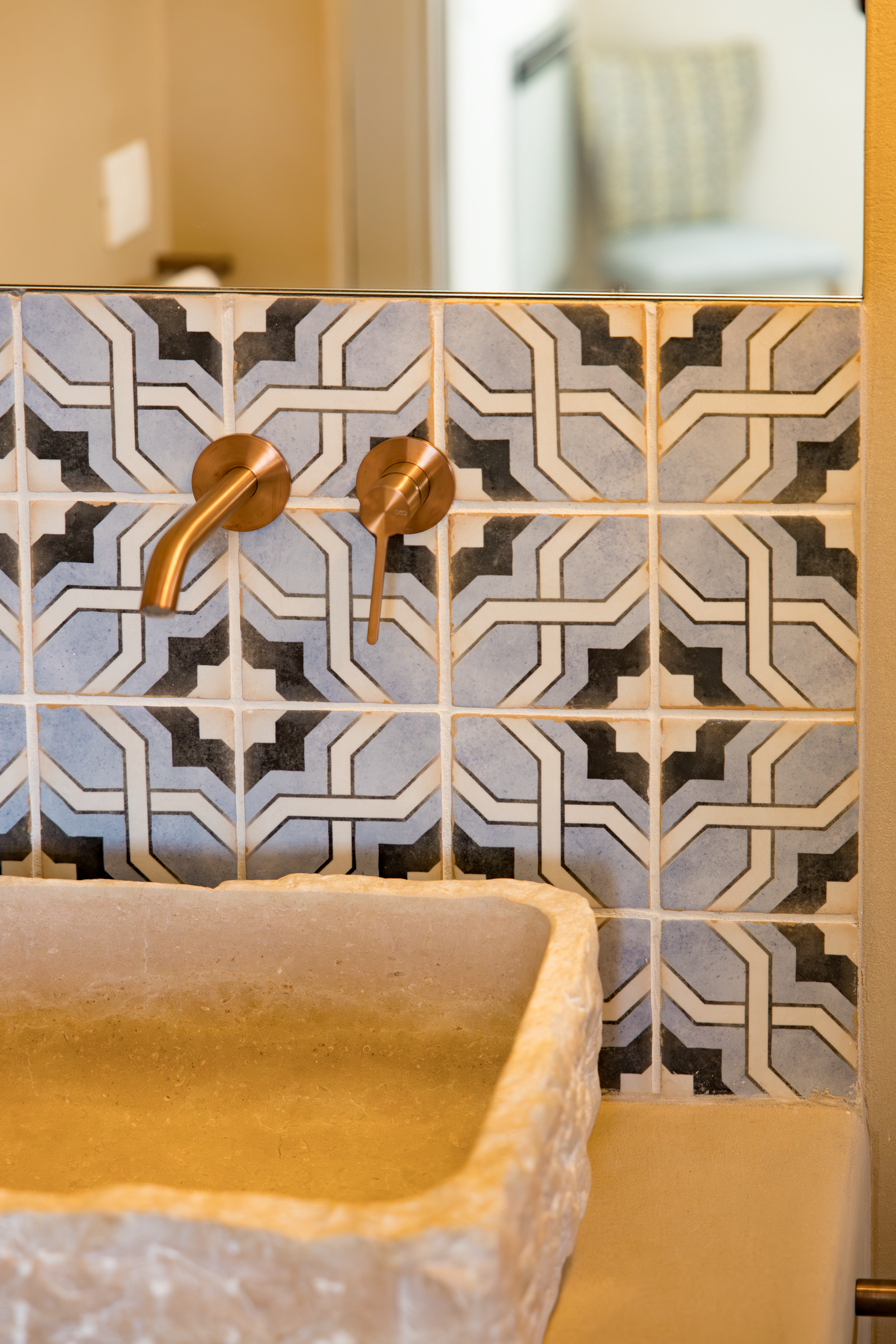 Close-up of brass wall-mounted taps and geometric patterned tiles above a stone sink in Puglia
