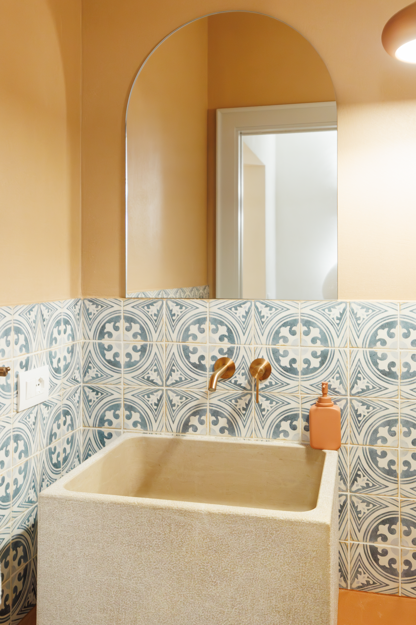 Stone washbasin with arched mirror and blue patterned tiles in a luxury villa bathroom in Puglia