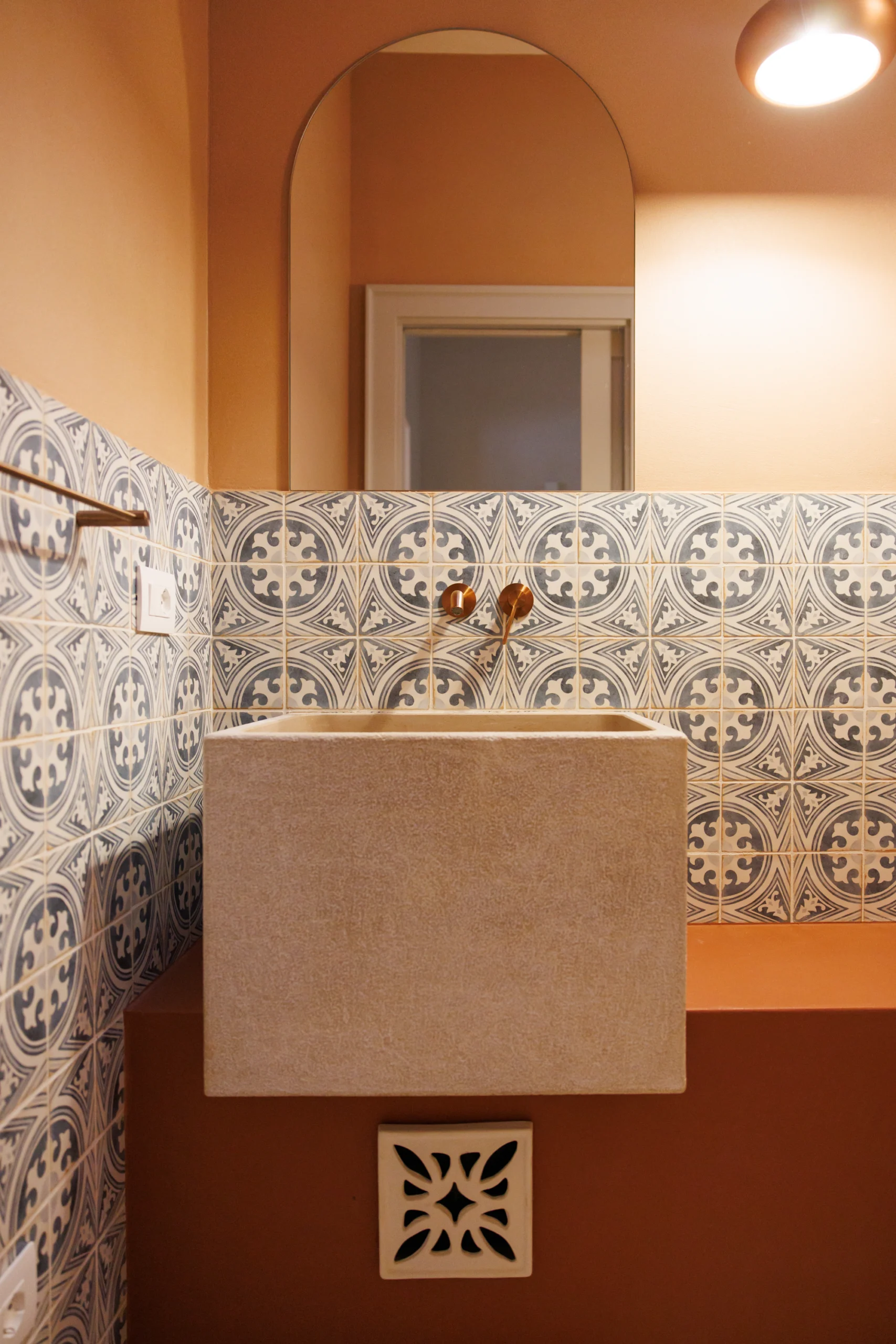 Elegant bathroom sink with patterned ceramic tiles, brass fixtures and arched mirror in Puglia