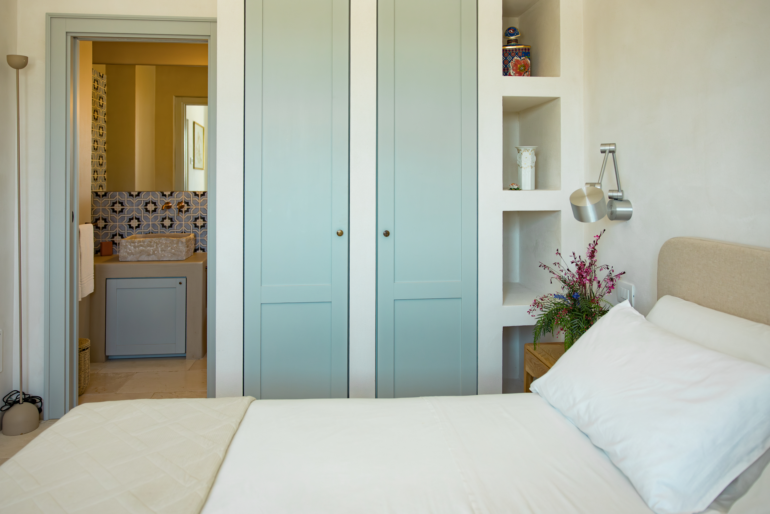 Bright bedroom with built-in wardrobe, soft linens and view toward bathroom in a Puglia villa