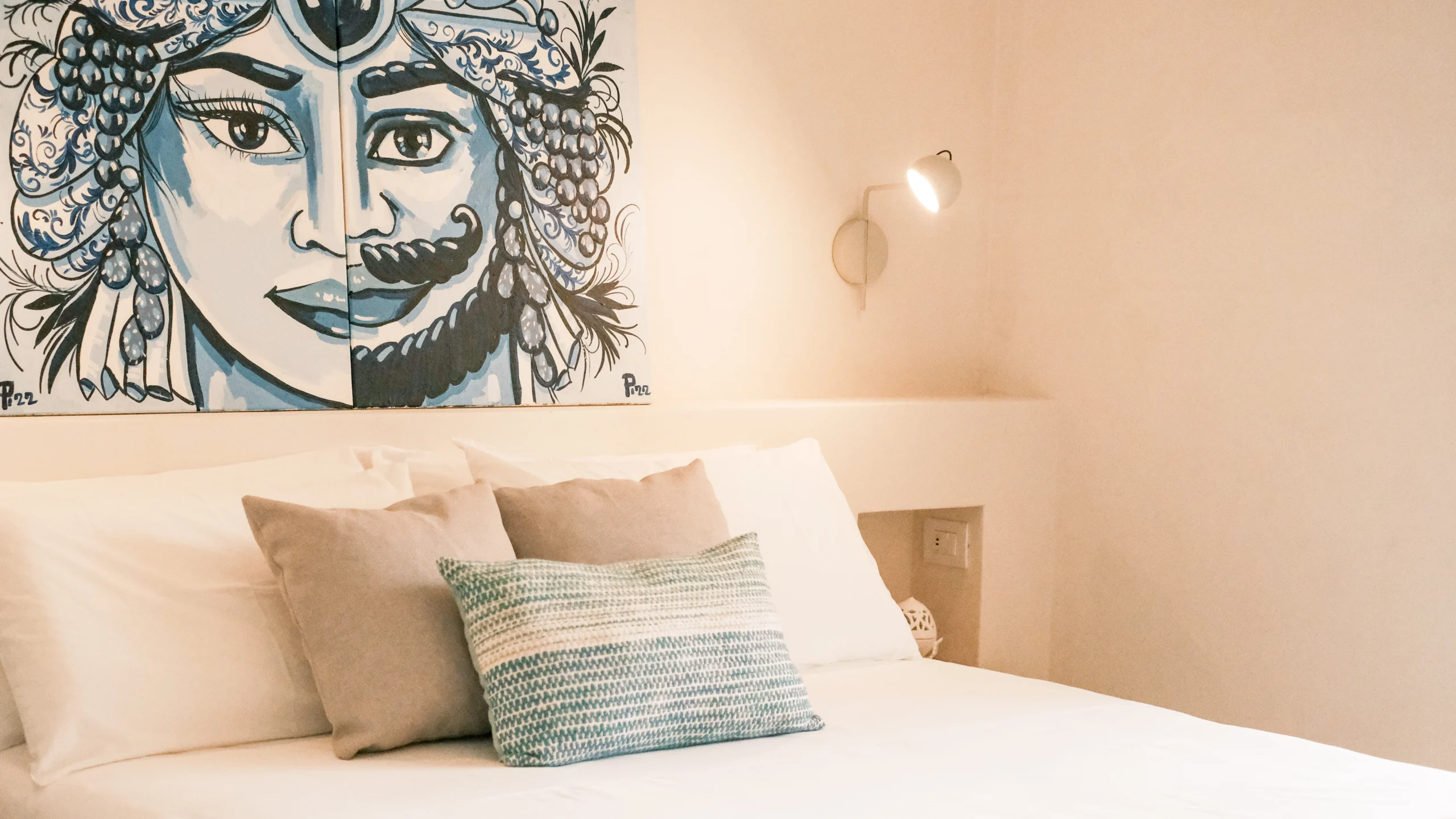 Luxury bedroom with artistic Sicilian-style wall art, soft textiles and designer wall lamp in Puglia