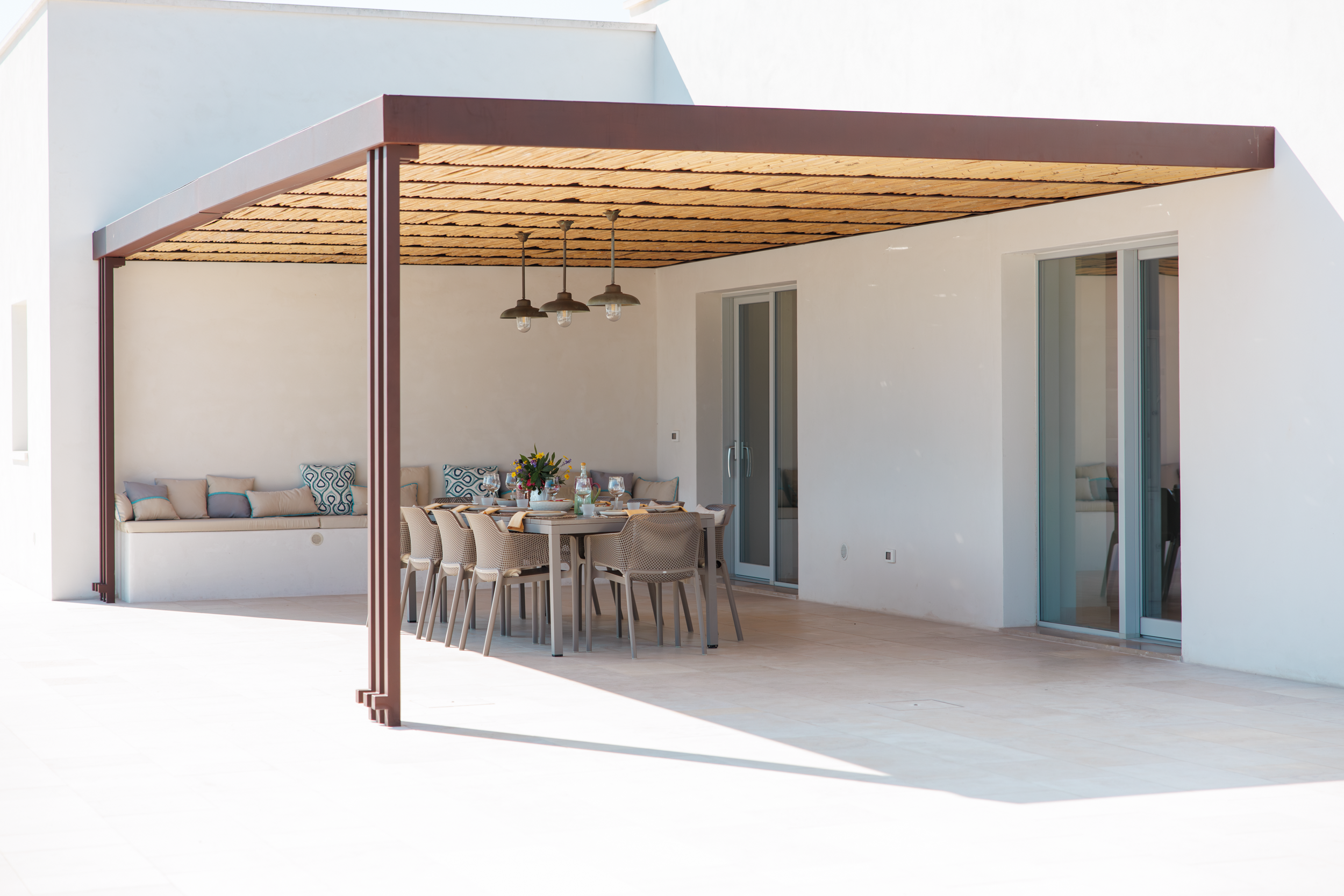 Covered outdoor dining area under a pergola with built-in bench and large table in a luxury villa in Puglia