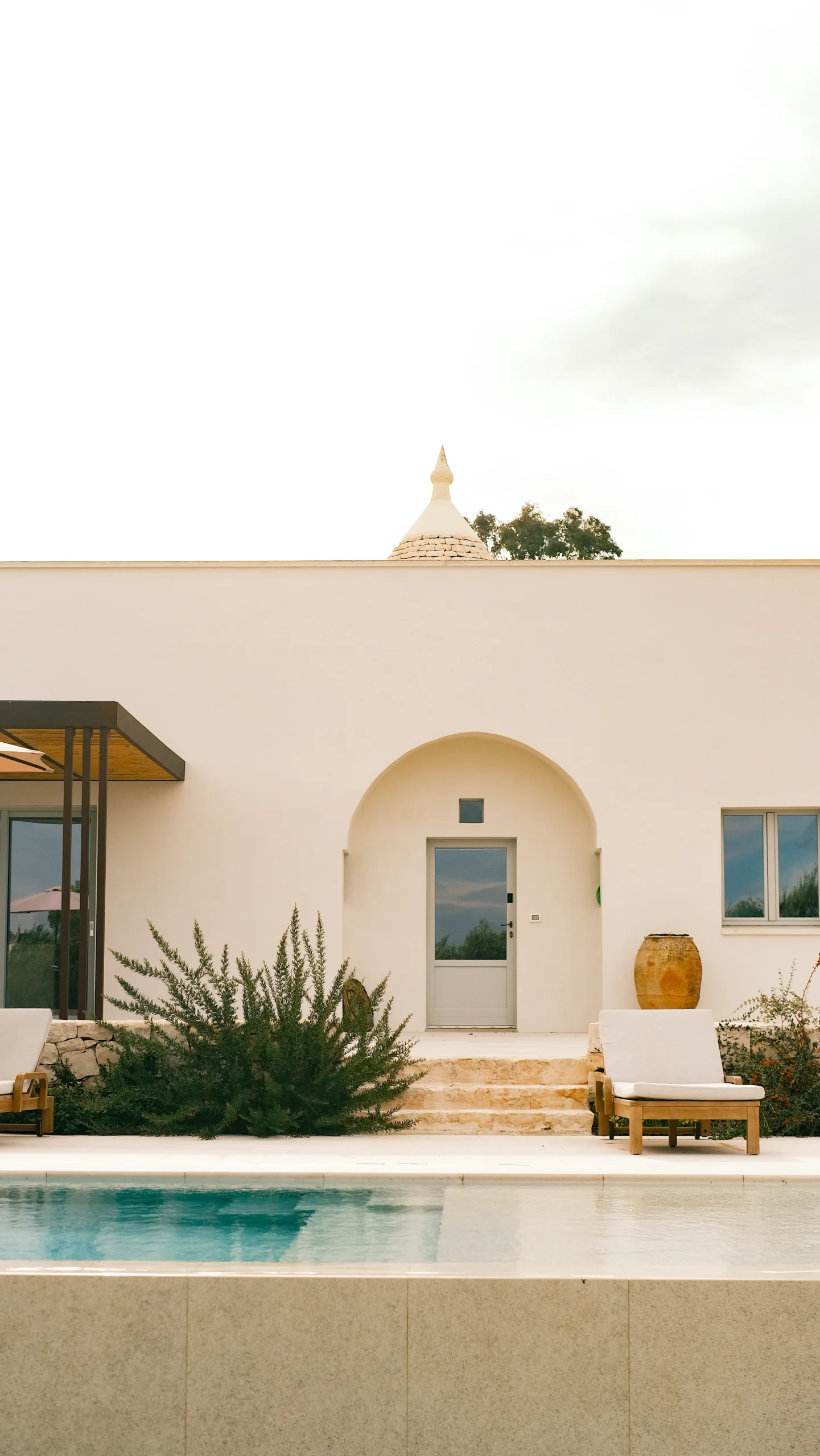 Minimalist villa entrance with arched doorway, stone steps and pool view in a luxury Puglia villa