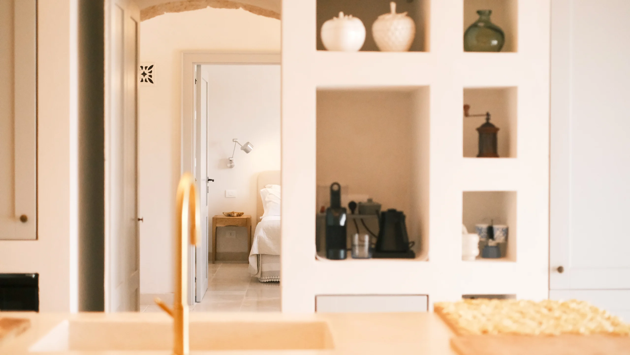 Bright open-plan kitchen with stone countertop, brass tap and custom built-in shelves in a luxury trullo villa in Puglia