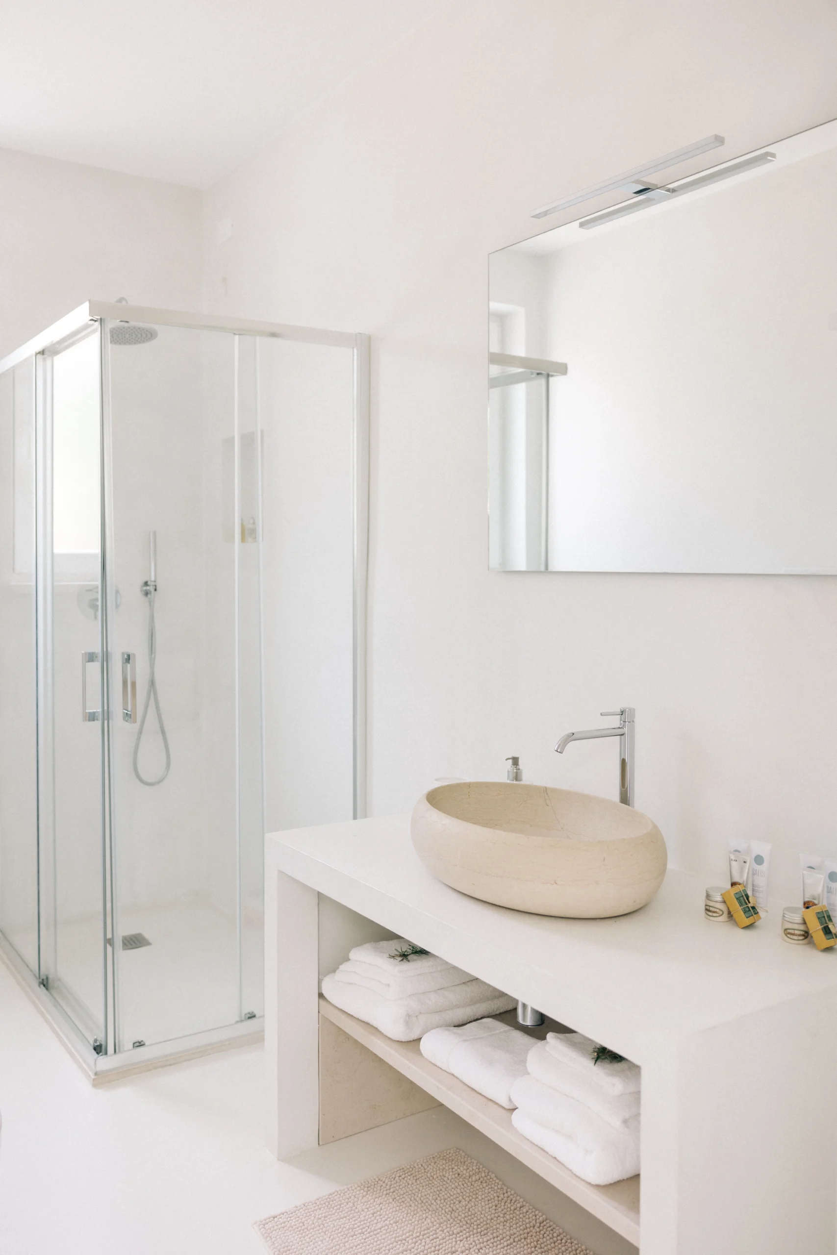 Villa Leucade contemporary bathroom with glass shower, beige stone finishes and designer washbasin.