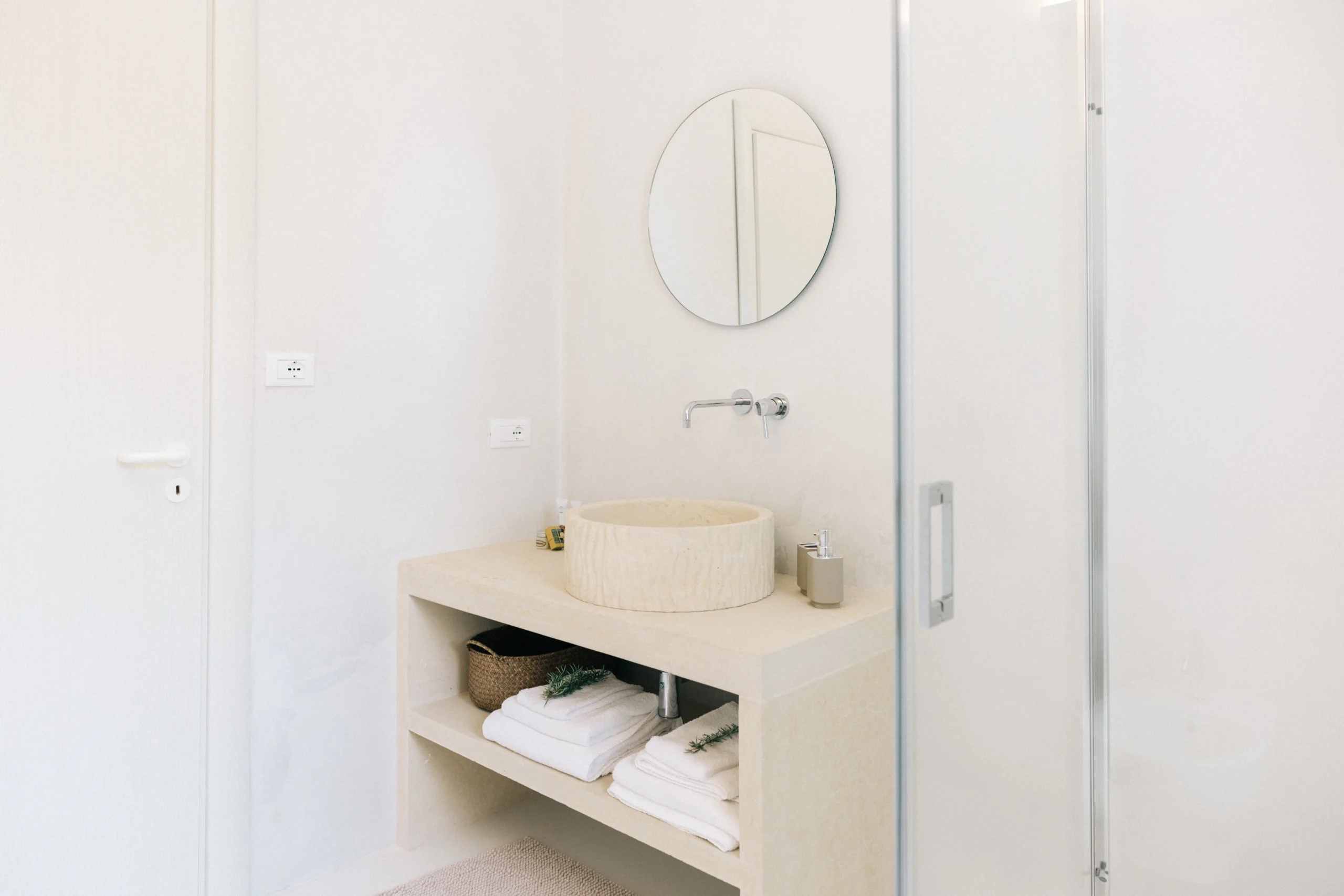 Villa Leucade bright bathroom with stone washbasin, open shelving and walk-in shower in modern Mediterranean style.