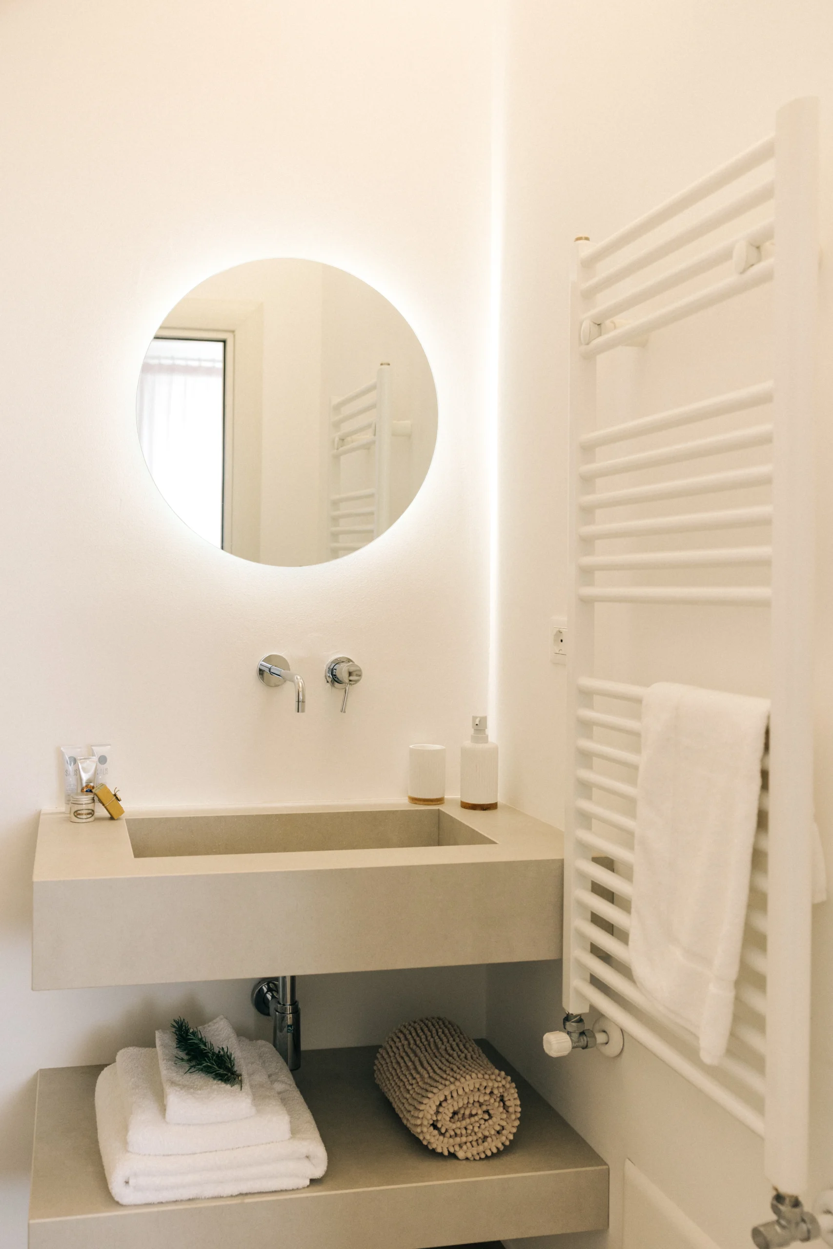 Villa Leucade bathroom with backlit round mirror, towel warmer and minimalist sink unit.