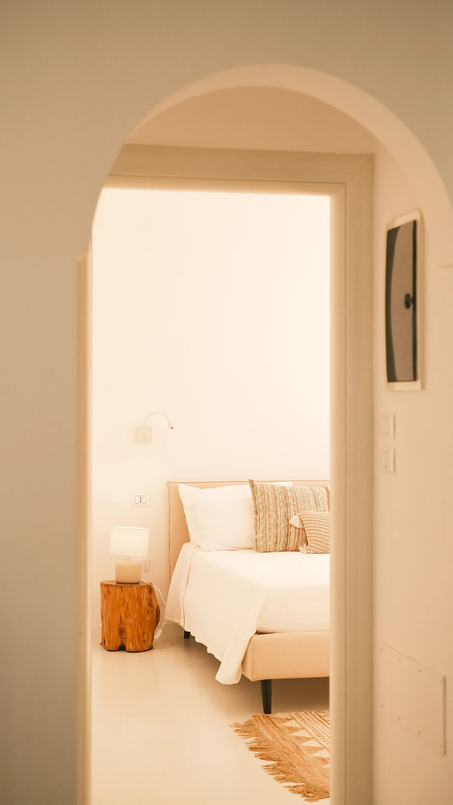 Arched doorway leading to bright minimalist bedroom with wooden bedside table and soft lighting