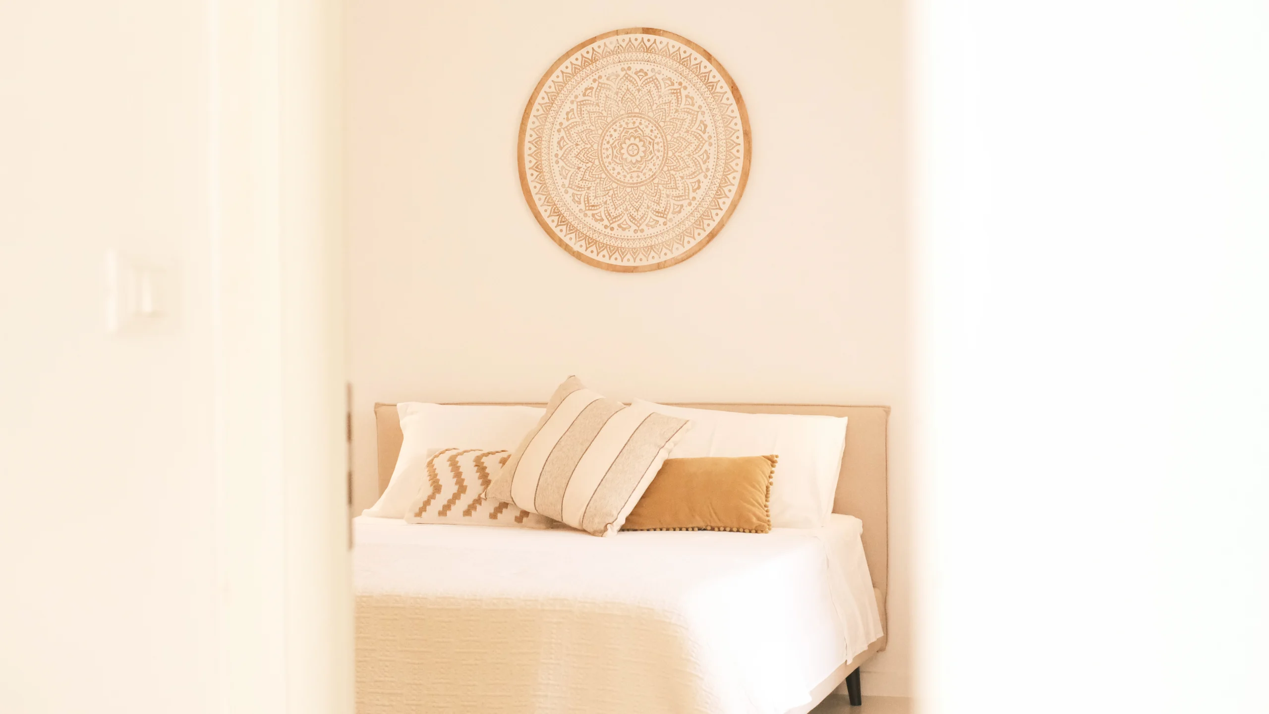 Soft-toned luxury bedroom with decorative mandala wall piece and designer cushions