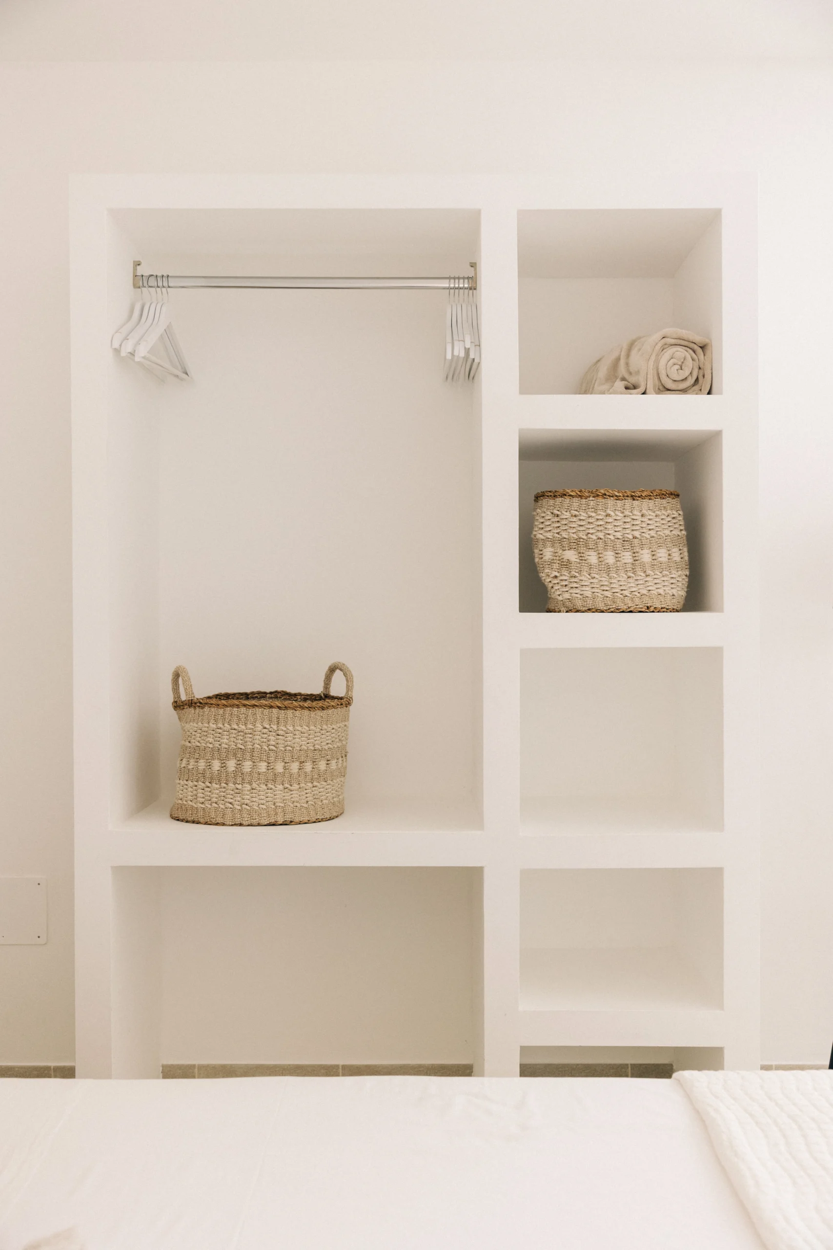 Built-in open wardrobe with shelves, hangers and woven baskets in luxury villa bedroom in Puglia.