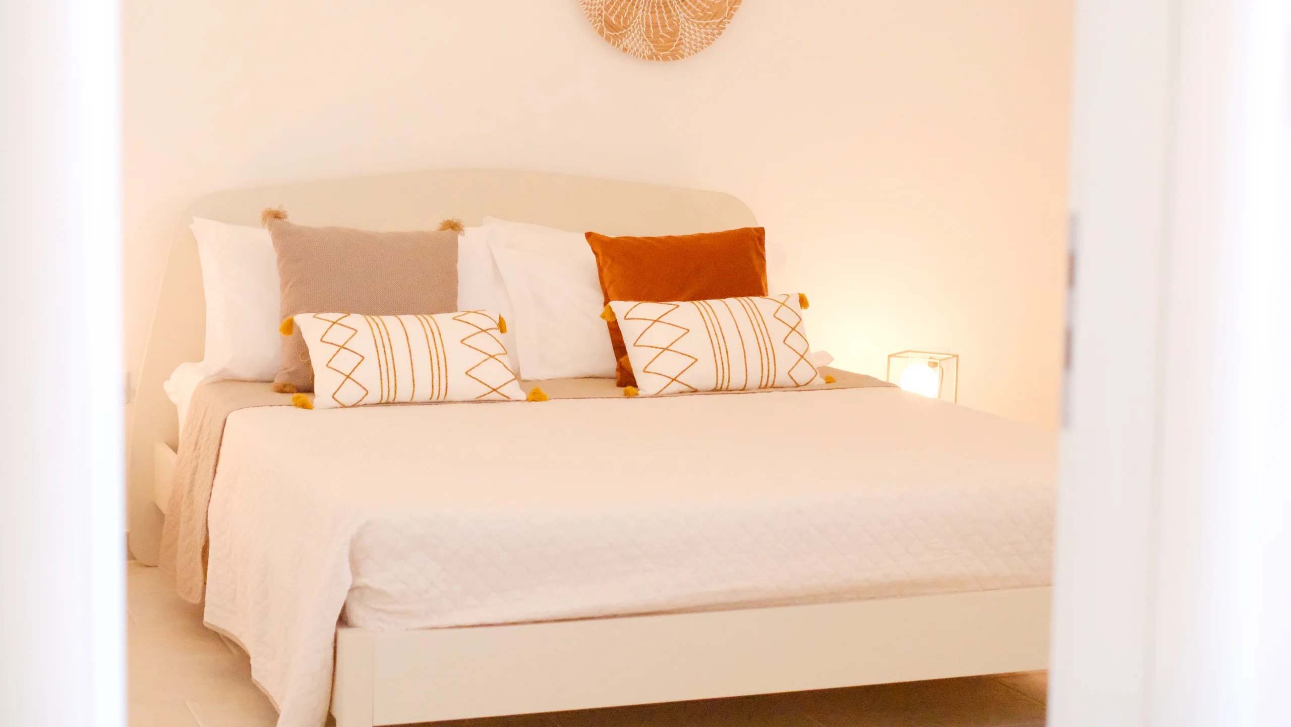 Elegant double bedroom at Villa Leucade with soft neutral tones, decorative cushions and warm ambient lighting.