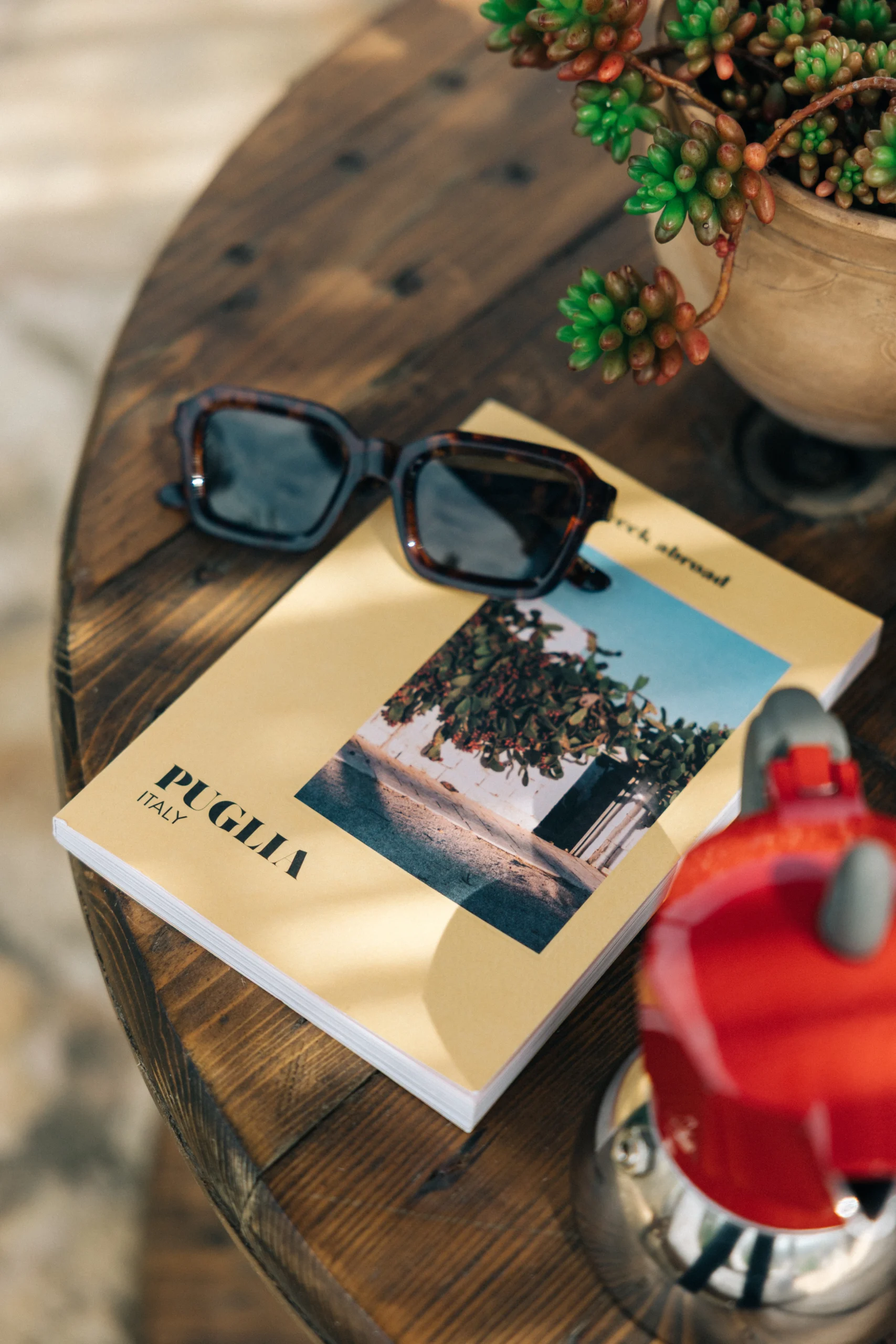 Lifestyle detail at Villa Leucade with Puglia travel book, sunglasses and espresso pot on wooden table.