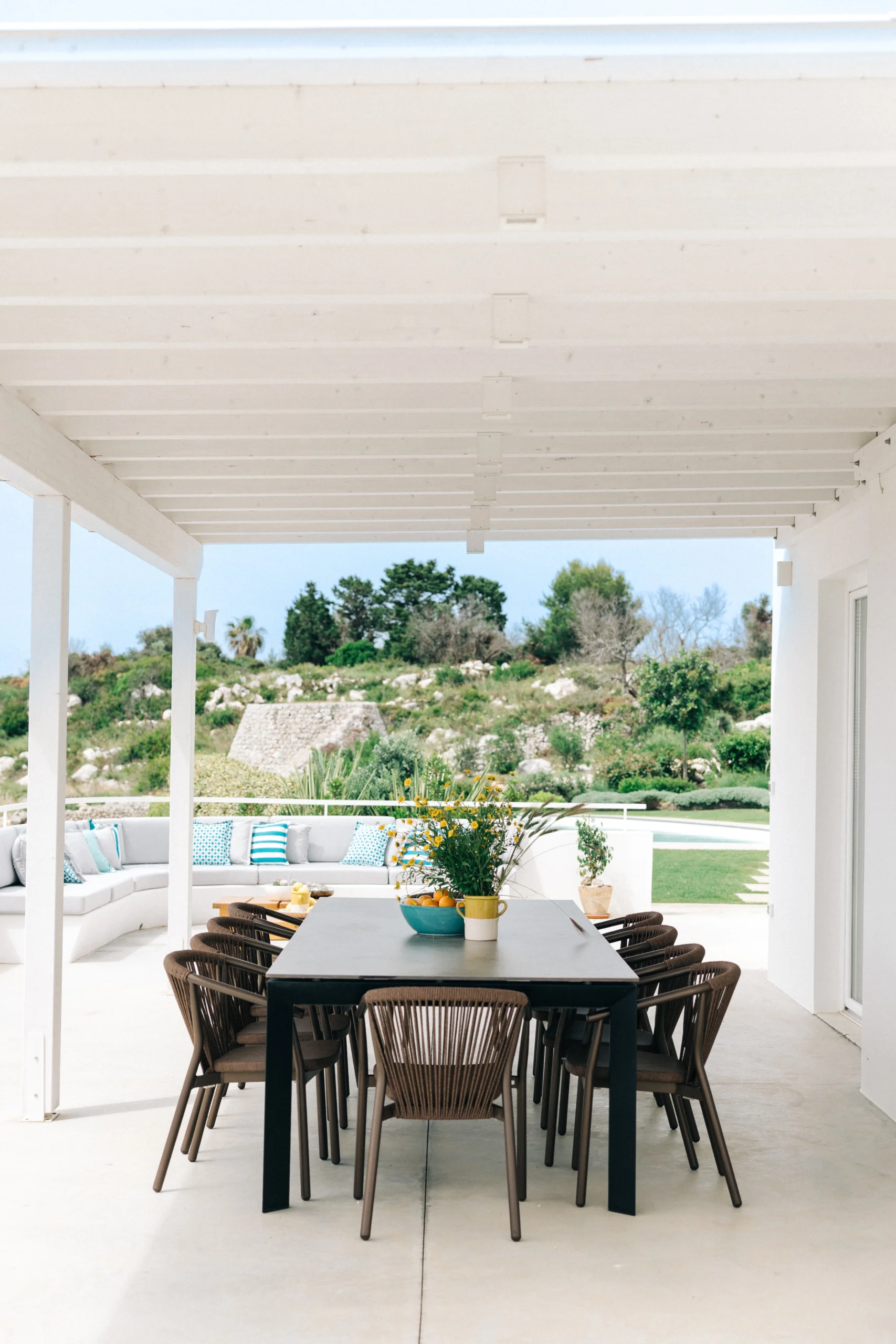 Outdoor dining area at Villa Leucade with shaded pergola, large table for guests and Mediterranean landscape view.