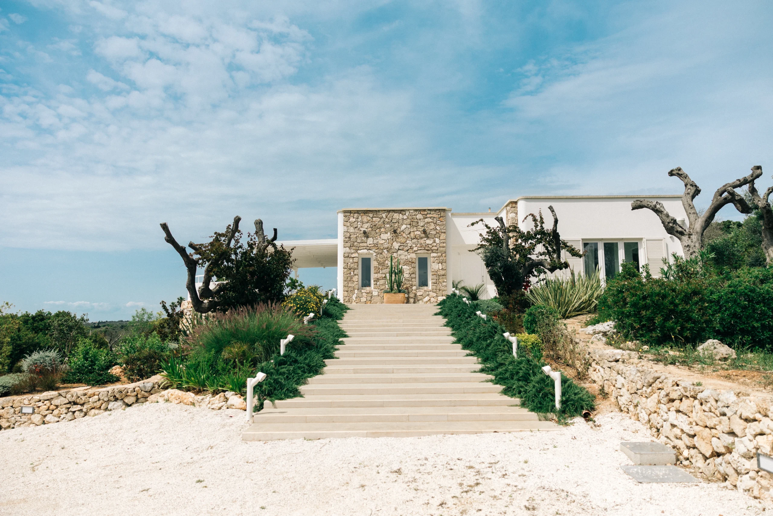 Main entrance of Villa Leucade with stone walls, landscaped garden and central staircase in luxury Puglia villa.