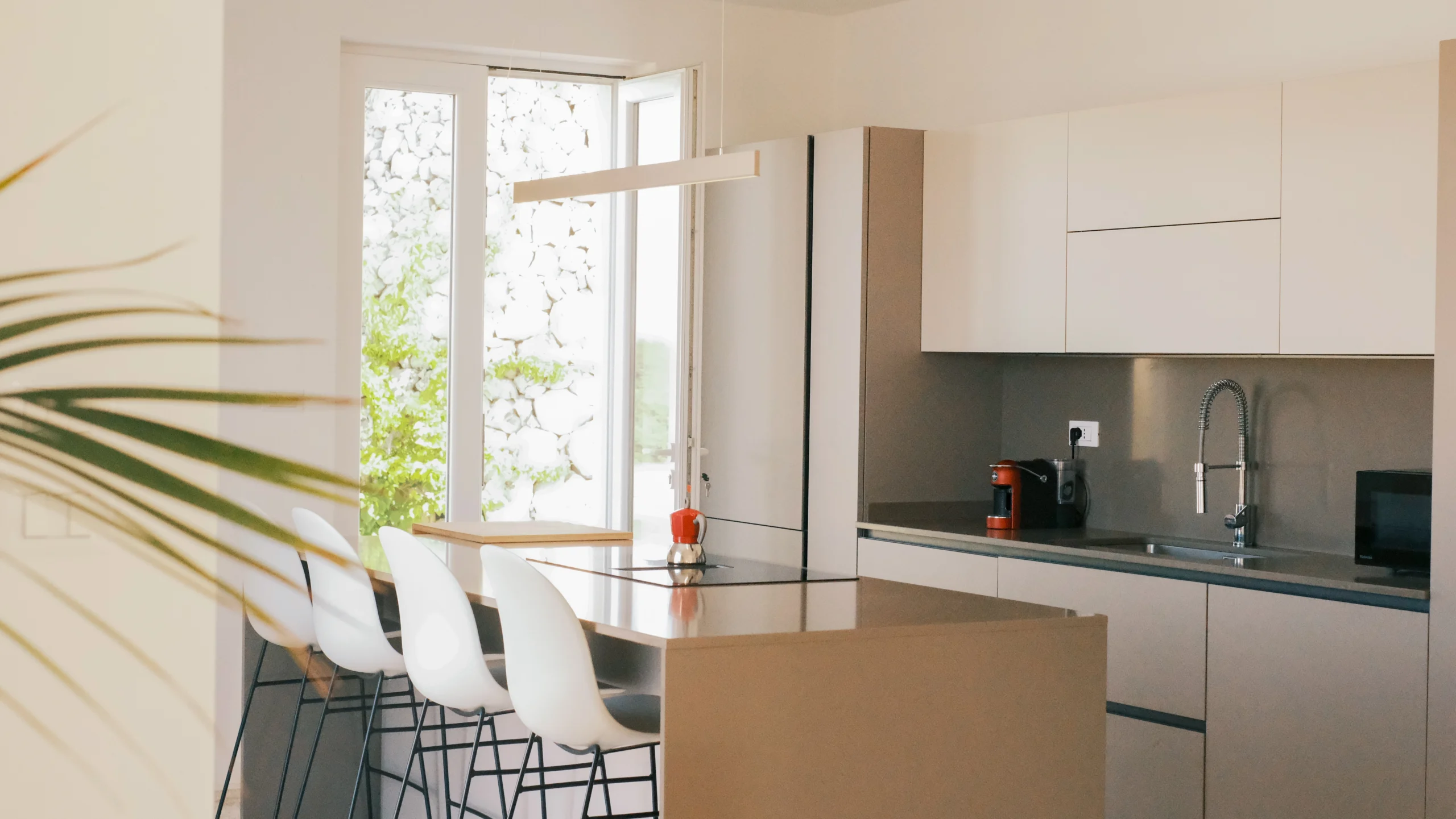 Bright designer kitchen at Villa Leucade with island seating, natural light and minimalist finishes in Puglia.