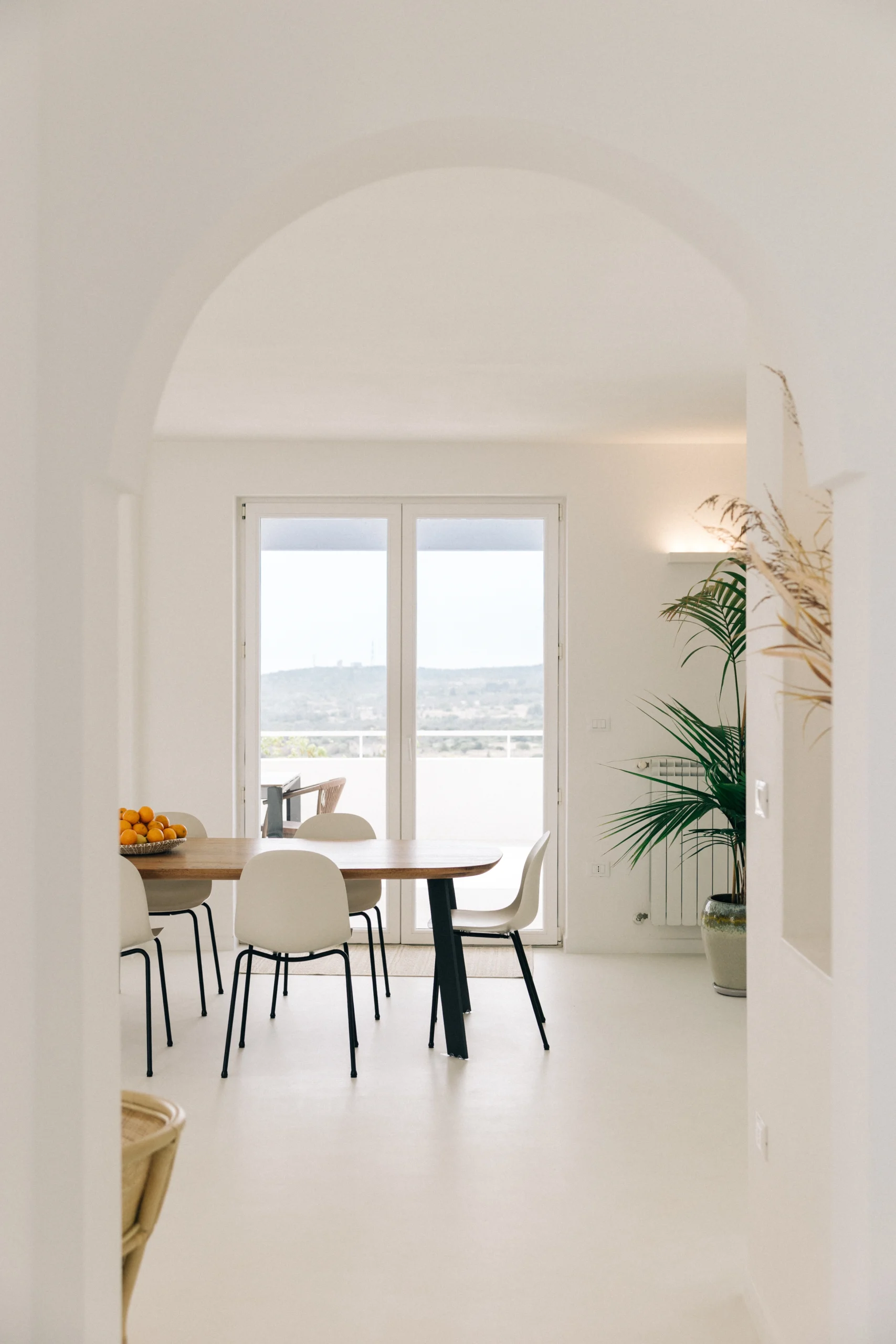 Elegant dining area with arched ceiling, white chairs and terrace access overlooking Puglia countryside
