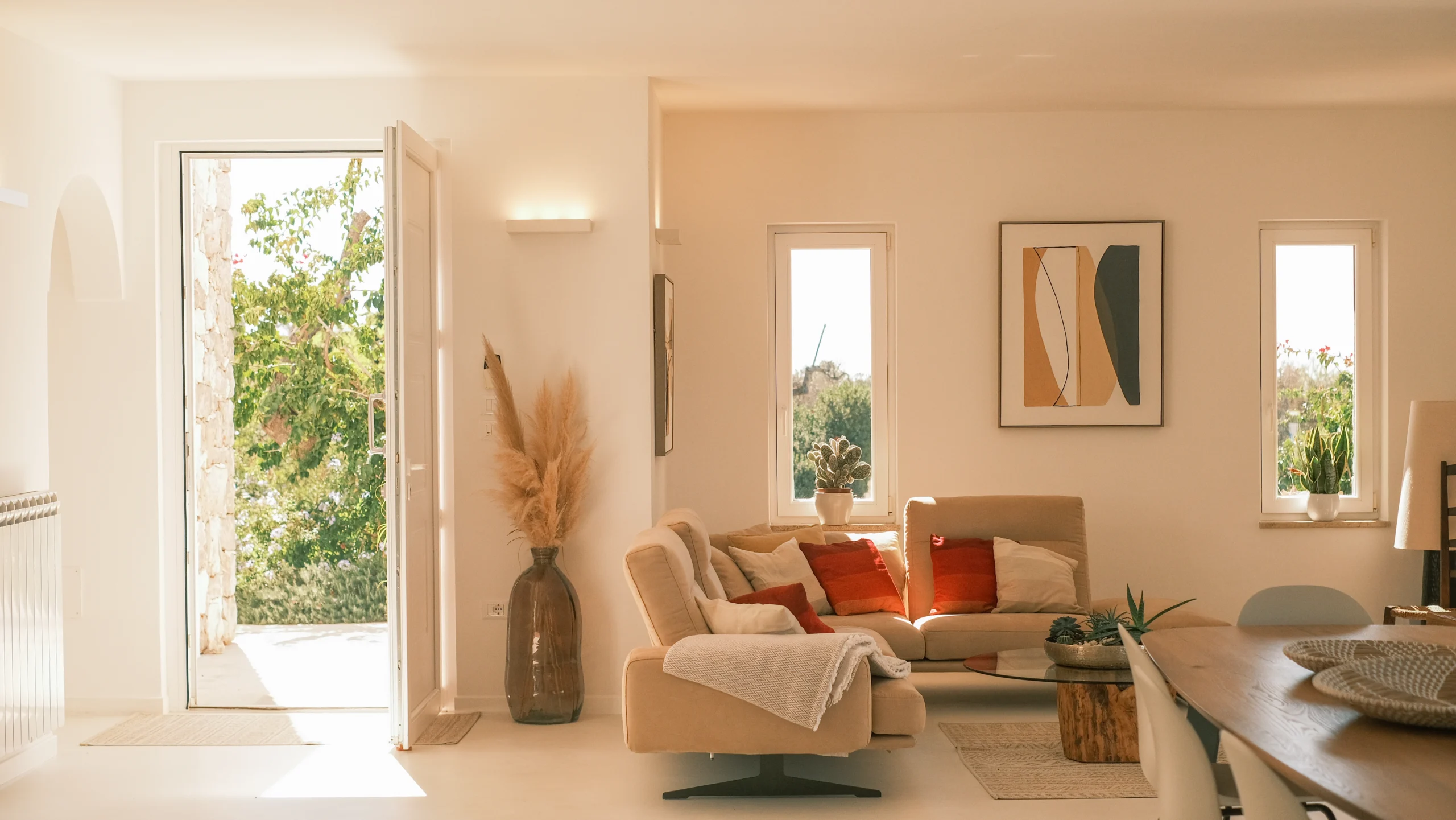 Bright modern living room with beige sofa, designer decor and open door leading to sunlit garden at luxury villa in Puglia