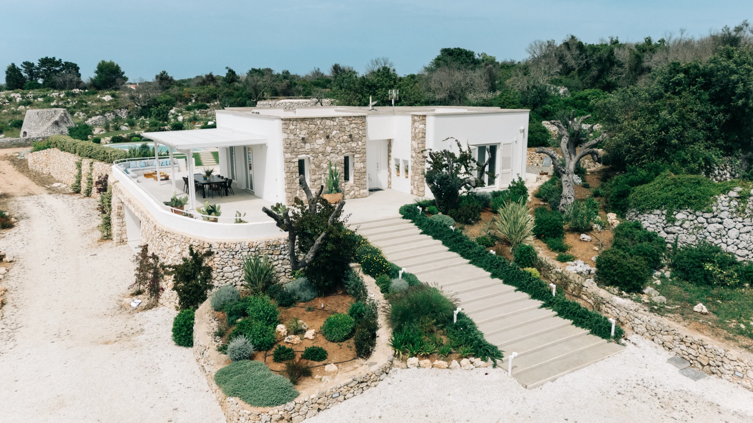 Front exterior view of luxury villa with stone walls, olive trees and elevated terrace in southern Italy