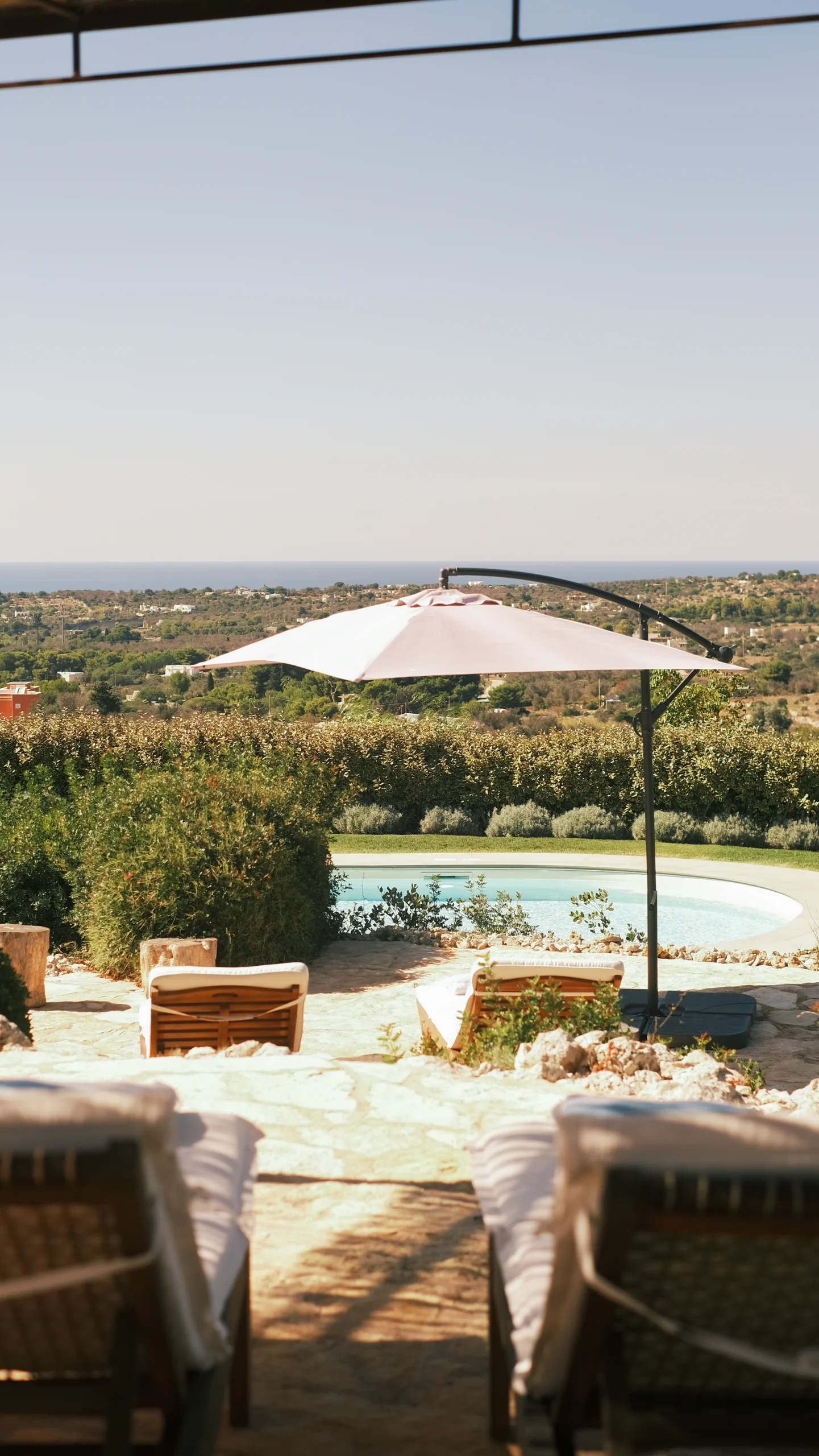 Luxury poolside sun loungers with parasol overlooking countryside and sea horizon in Puglia