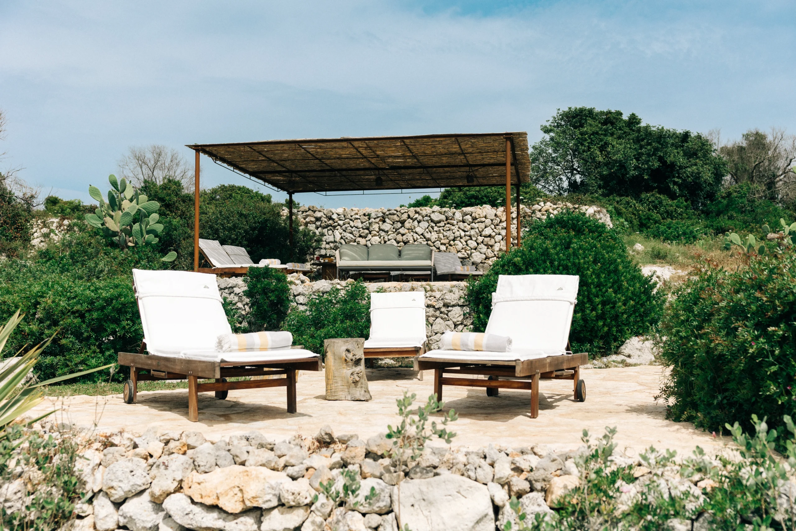 Shaded pergola lounge with outdoor sofas surrounded by Mediterranean garden at private villa in Puglia