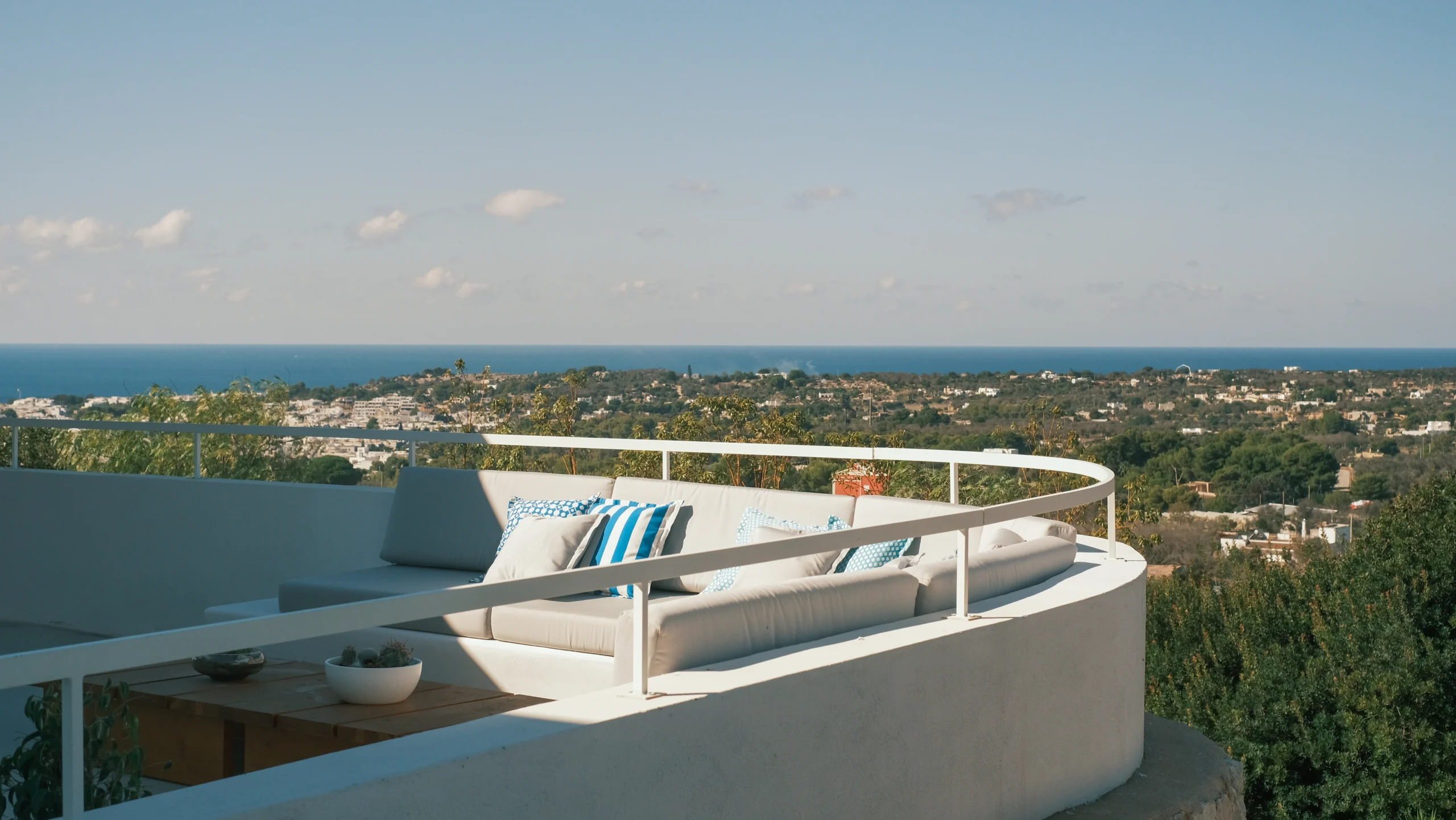 Rooftop terrace lounge with curved sofa and panoramic sea views over the Puglia countryside