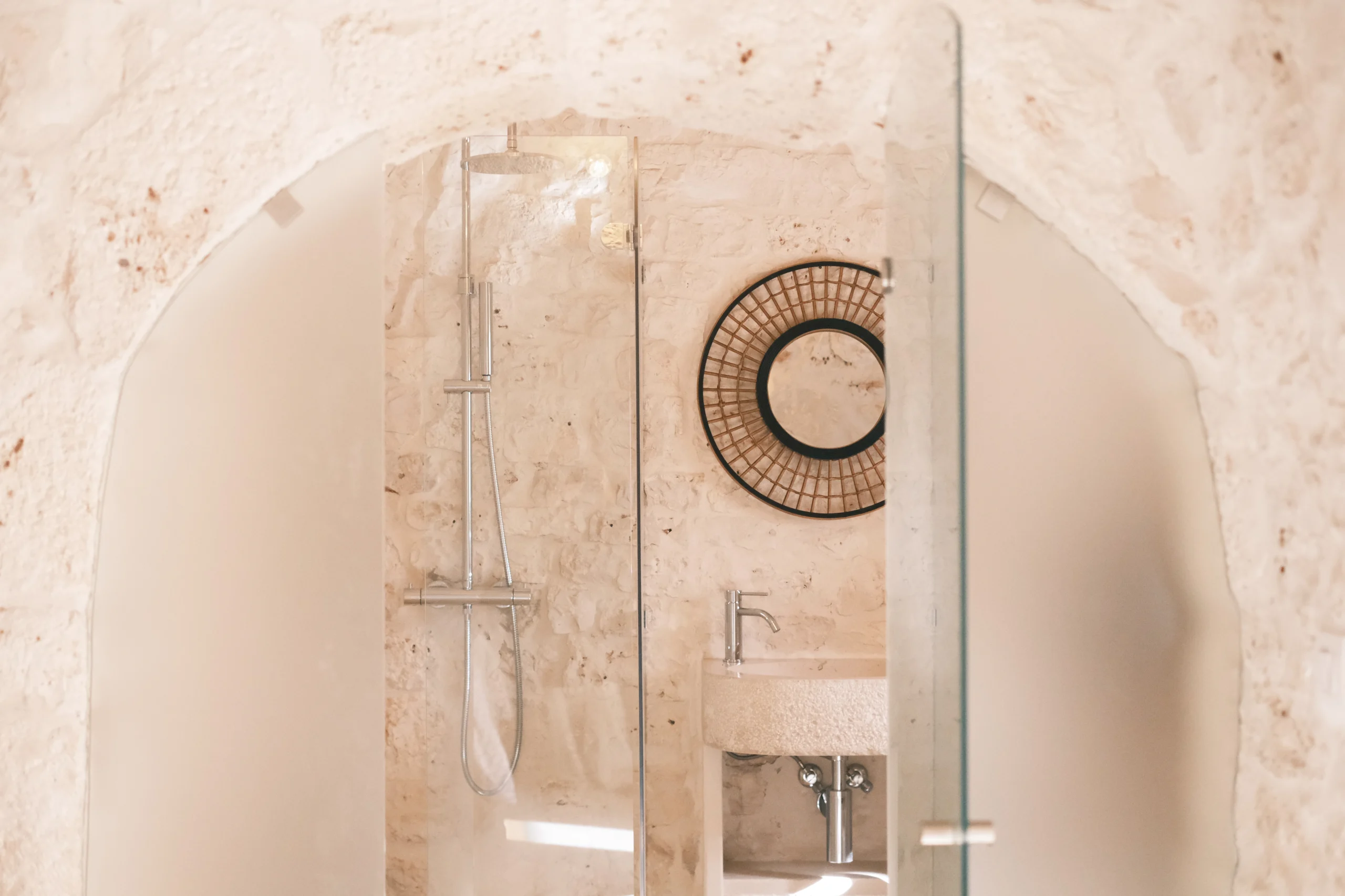Arched stone bathroom featuring a glass shower and minimalist stone basin in a luxury villa in Puglia