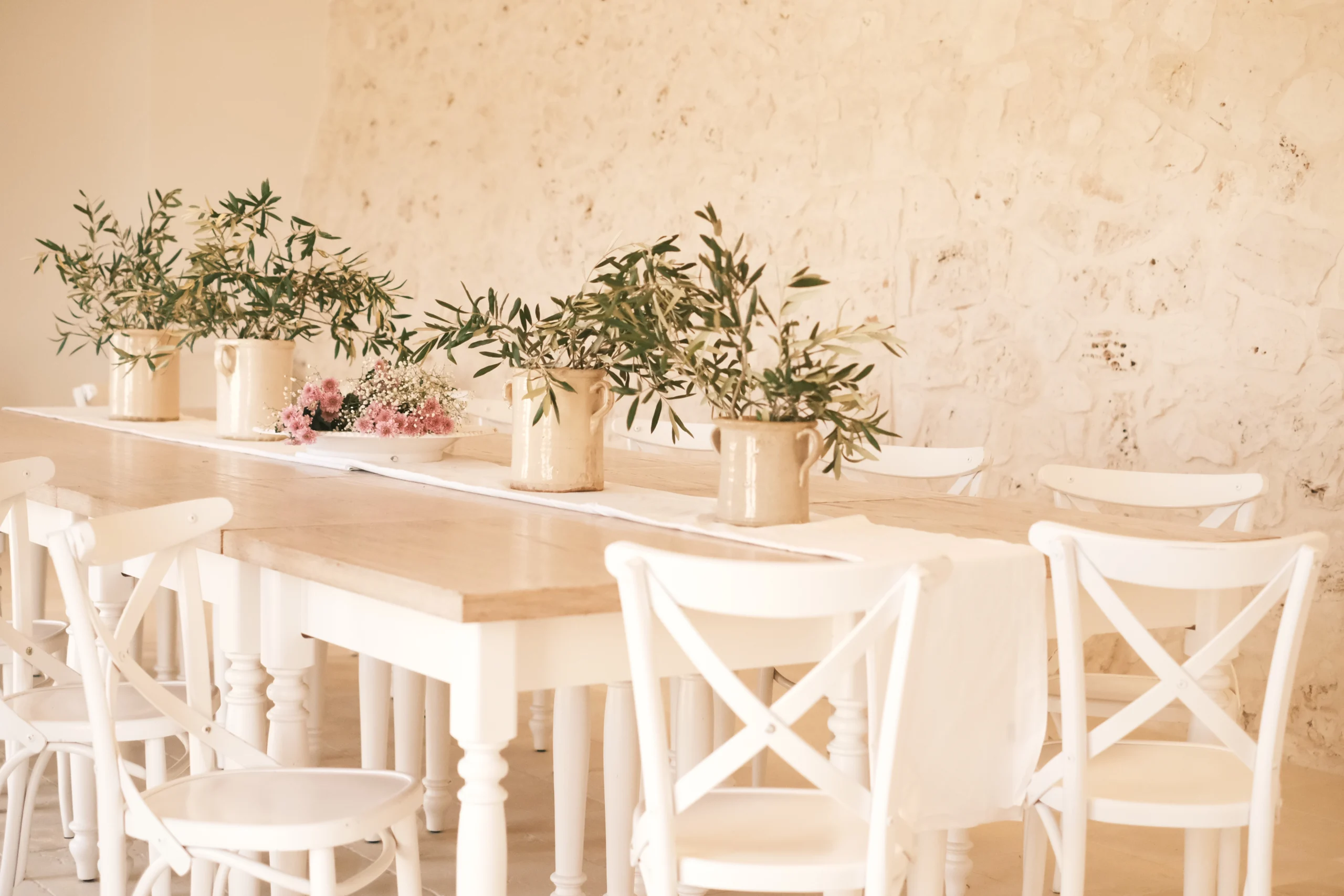 Bright dining room with rustic wooden table, white chairs and olive branches in ceramic vases at a luxury villa in Puglia