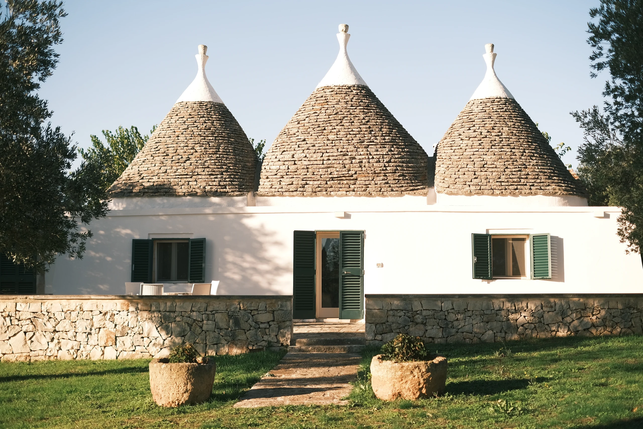 Traditional trullo house with three stone cone roofs surrounded by olive trees in the Puglia countryside