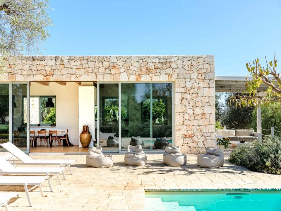 Stone villa exterior with turquoise pool, bean bag chairs and sun loungers on limestone terrace in Puglia
